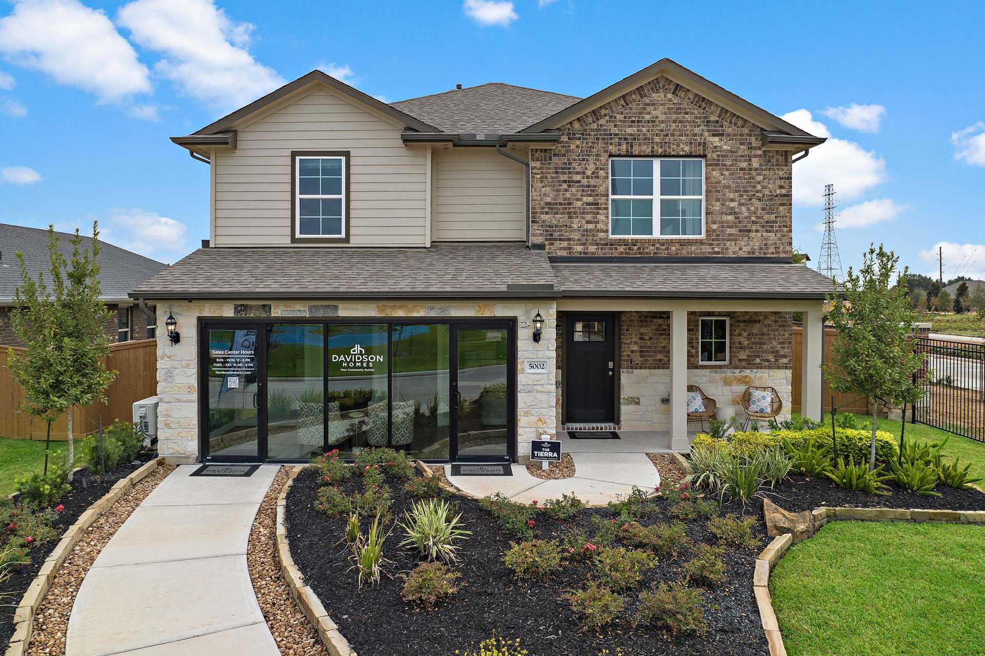 Contemporary two-story home exterior at Sunterra in Katy Texas with brick stone facade covered porch and landscaped yard