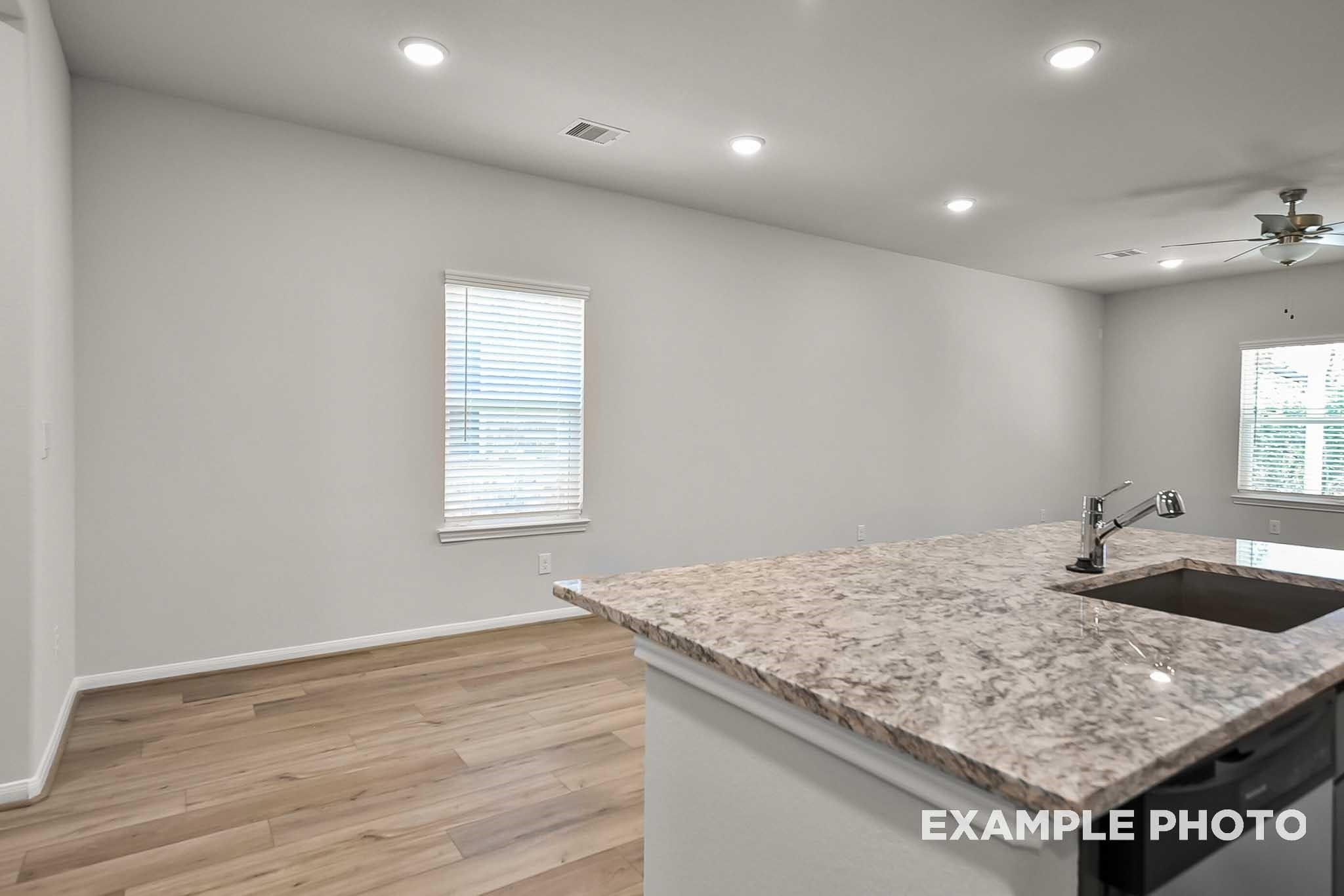 Modern kitchen with granite island and light wood flooring in The Blanco F floor plan at Spring Branch Crossing, Conroe.