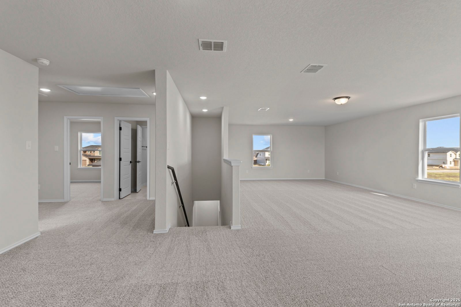 Spacious upstairs hallway with gray carpet, bedroom doors, staircase, and large windows in Davidson Homes Douglas C, Seguin, Texas