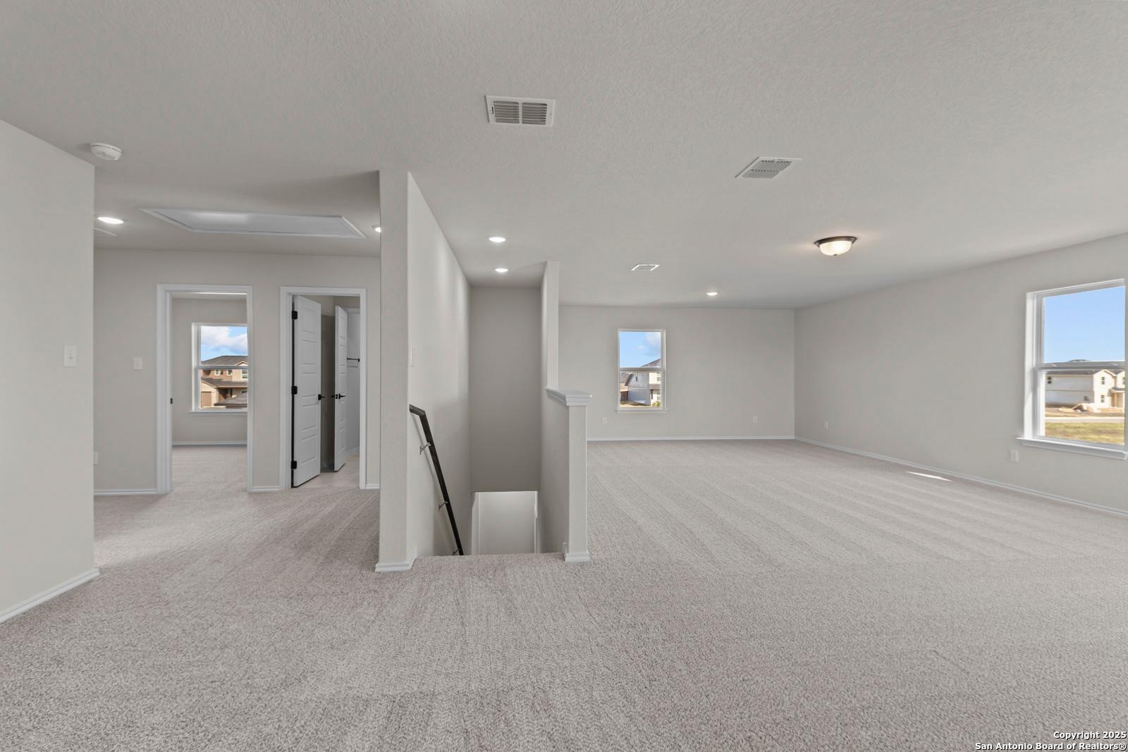 Spacious upstairs hallway with gray carpet, bedroom doors, staircase, and large windows in Davidson Homes Douglas C, Seguin, Texas