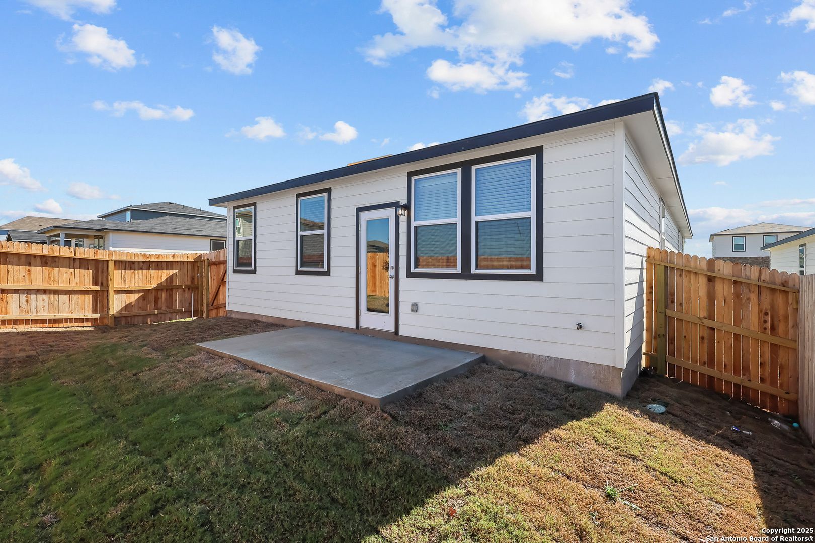 Modern white single-story home with black-trimmed windows, concrete porch, and fenced grassy yard in Davidson Homes The Colorado B, San Antonio
