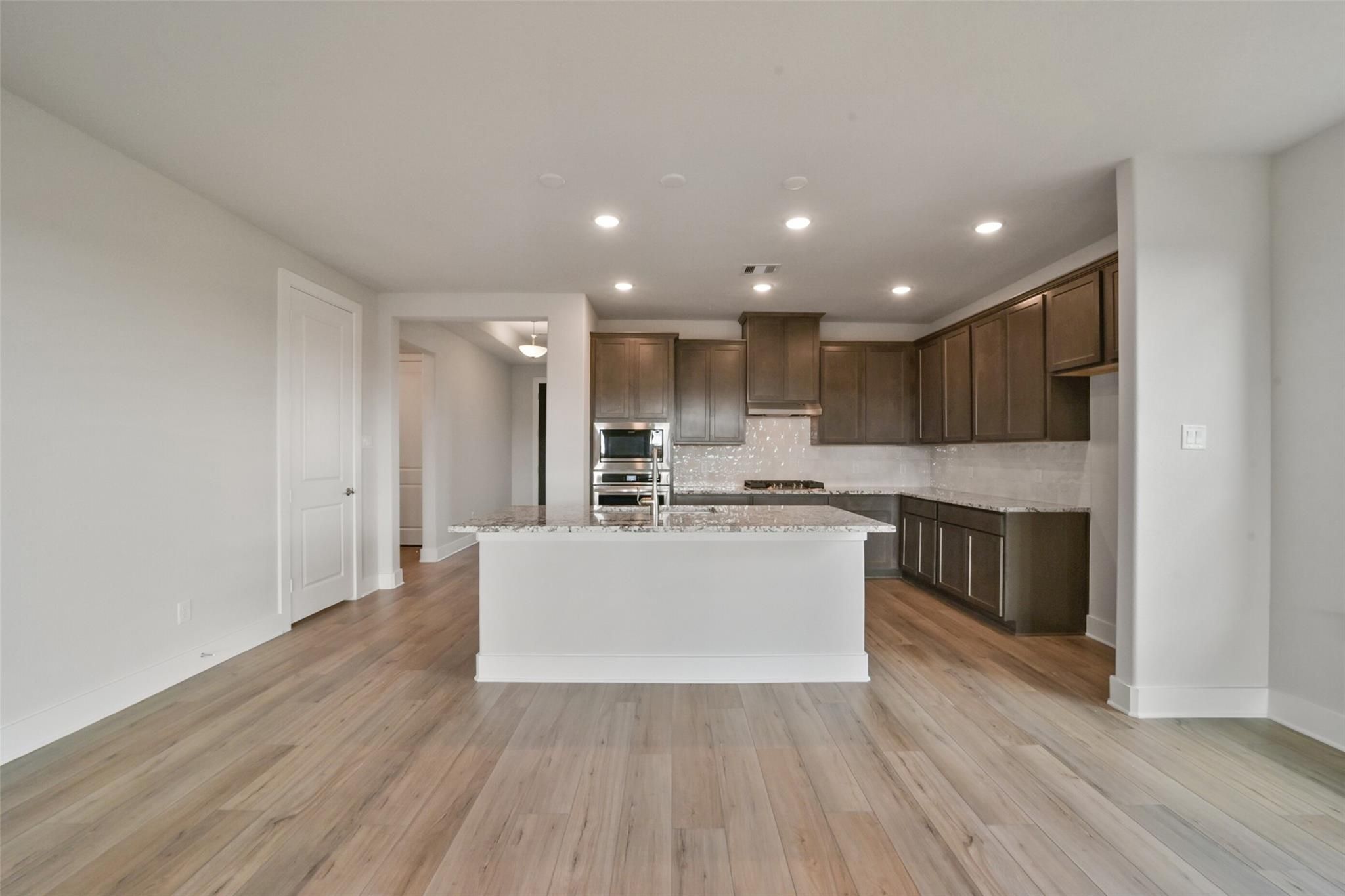 Open-concept kitchen with white quartz island, dark wood cabinets, stainless double oven, hardwood floors in Davidson Homes The Zion A, Lago Mar