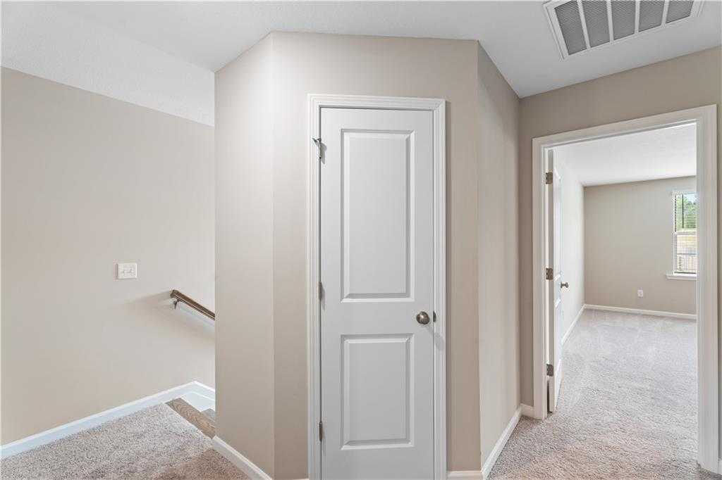 Upper-level hallway featuring beige carpeted floors, white doors, and staircase in Davidson Homes The Bartlett, Phenix City, Alabama