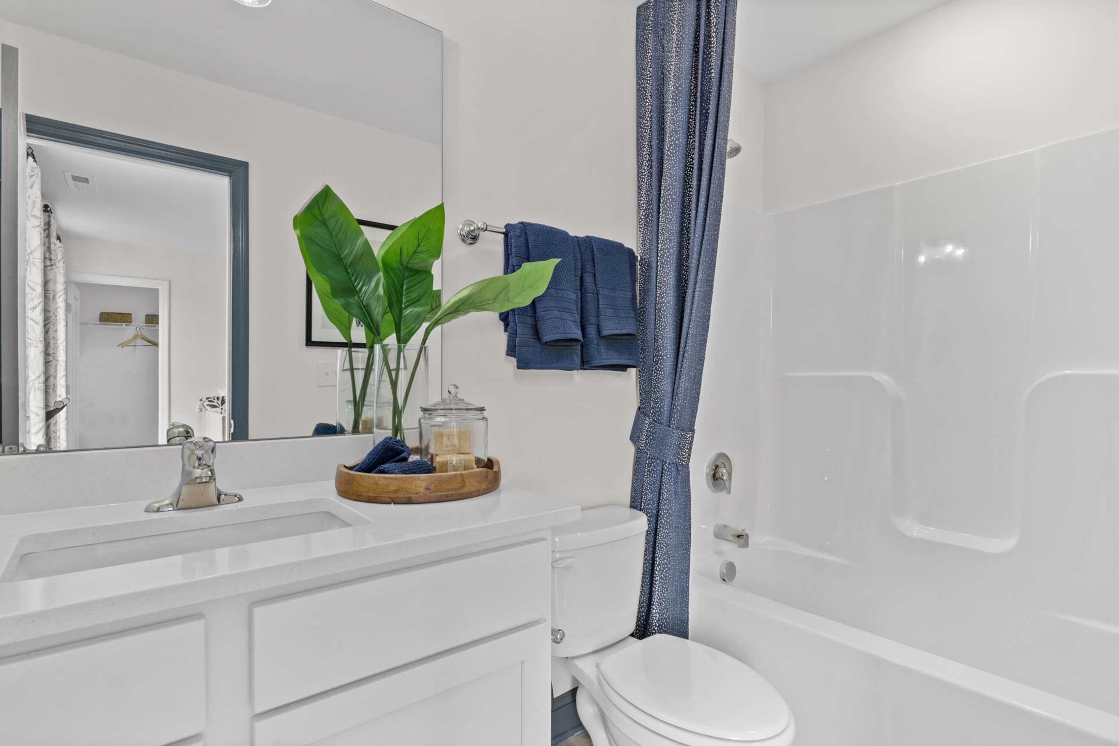 Modern bathroom at Creek Grove in New Market Alabama with white vanity, blue towels, potted plant, and bathtub