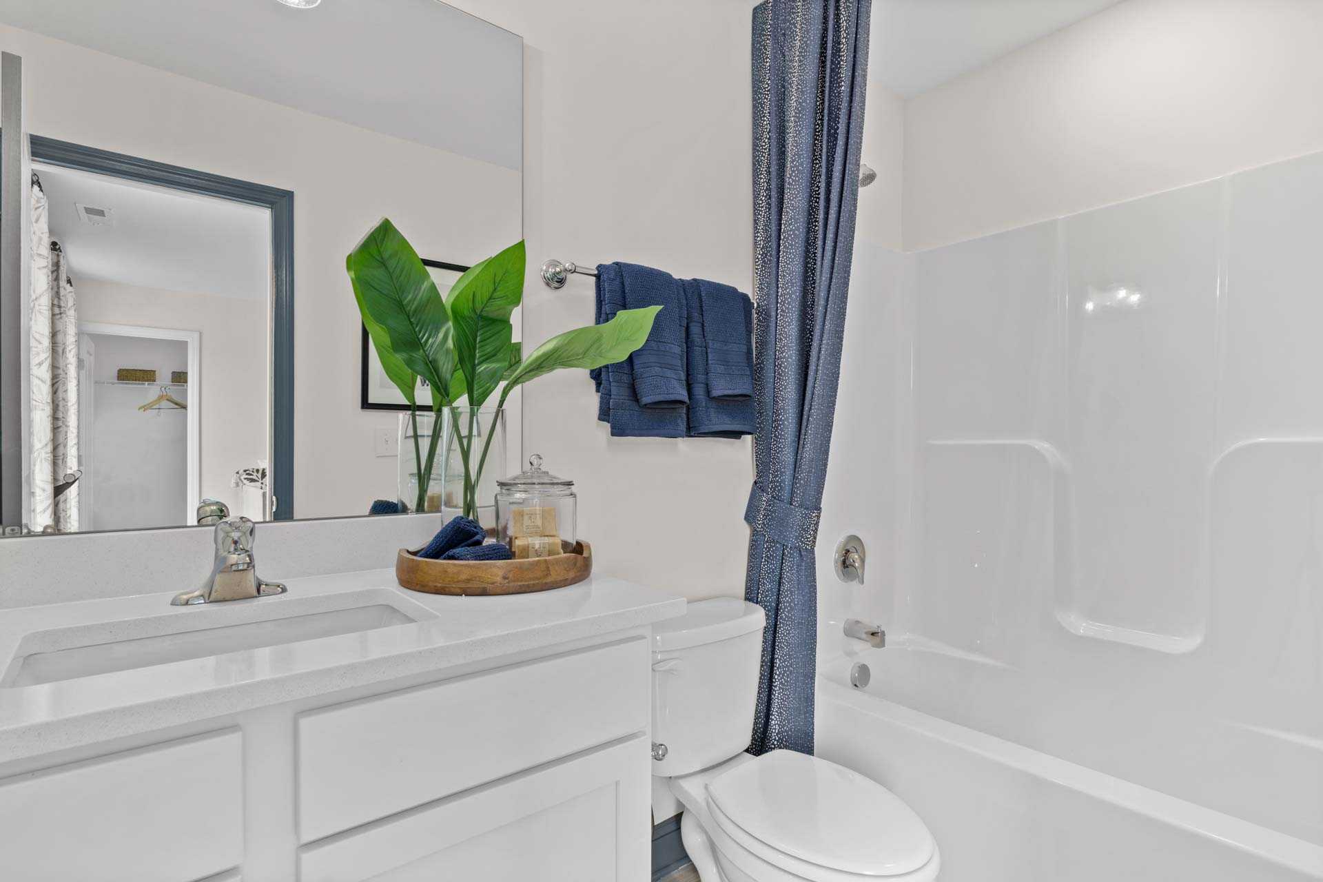 Modern bathroom at Creek Grove in New Market Alabama with white vanity, blue towels, potted plant, and bathtub