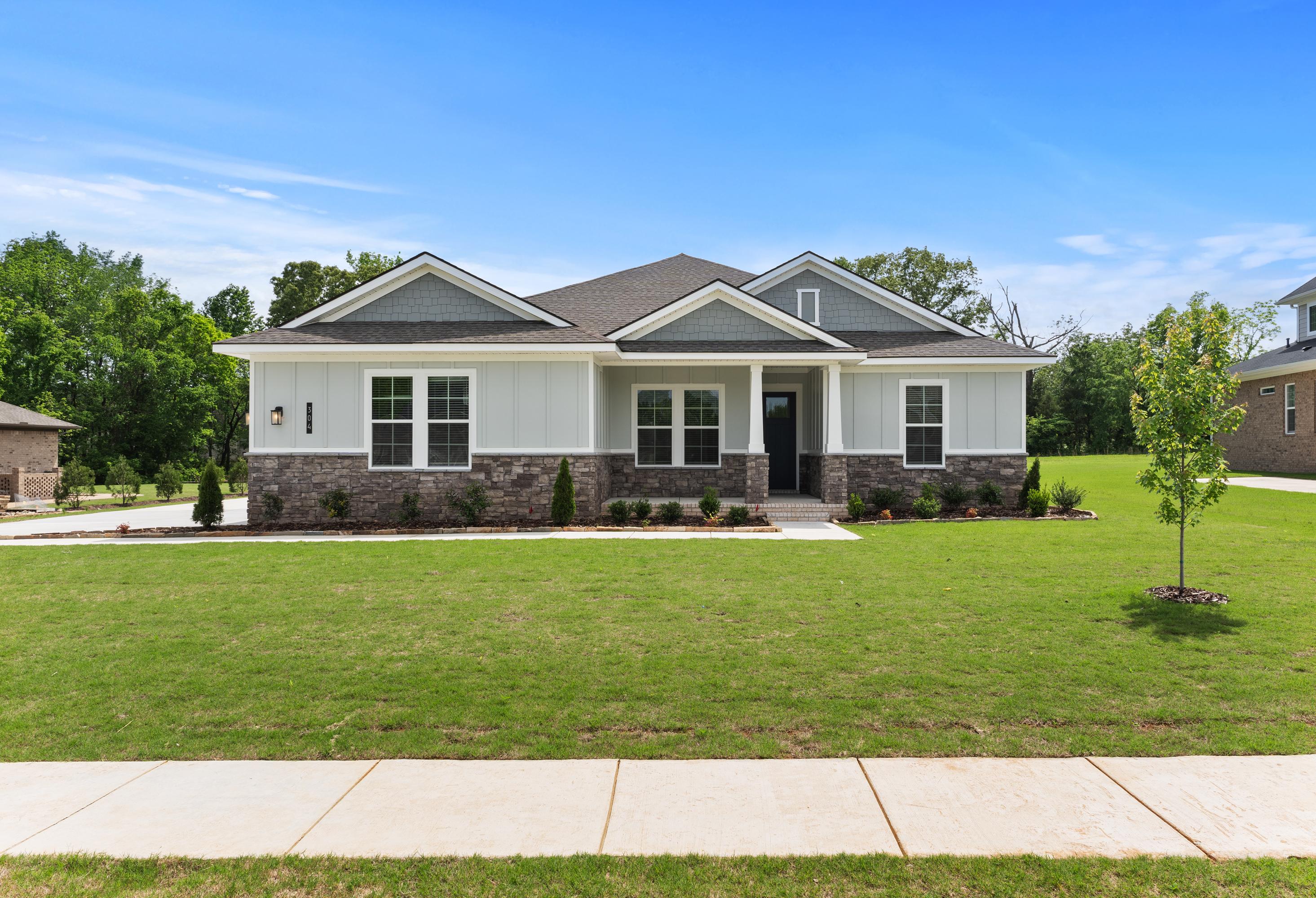 Modern ranch-style front elevation of The Arcadia B with gray siding, brick base, large windows, and lush green lawn