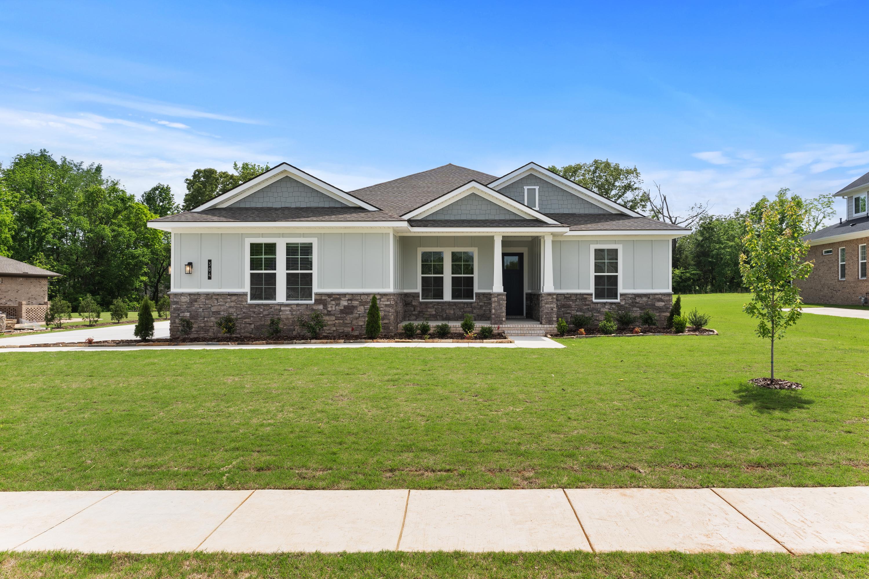 Modern ranch-style front elevation of The Arcadia B with gray siding, brick base, large windows, and lush green lawn