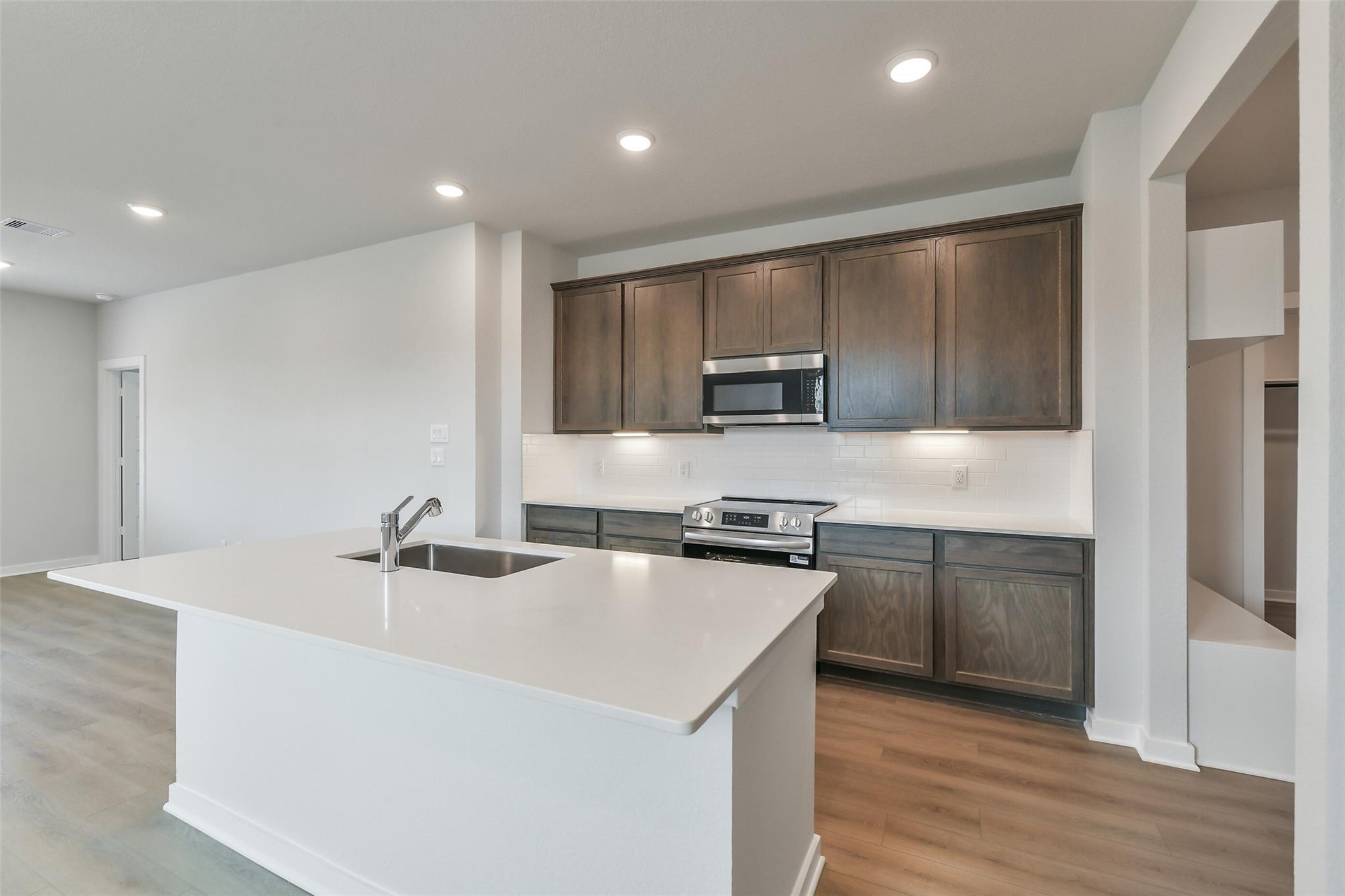 Modern kitchen with white quartz island, shaker dark cabinets, stainless appliances in Davidson Homes The Brazos E, Cleveland TX