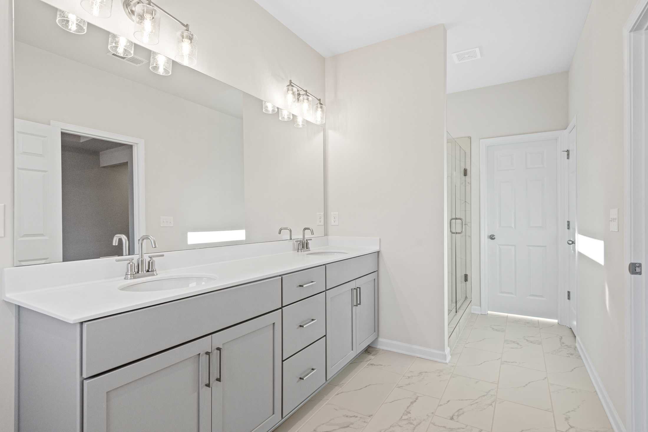 Spacious master bath in The Glenwood A with double vanity, gray shaker cabinets, quartz counters, and frameless shower