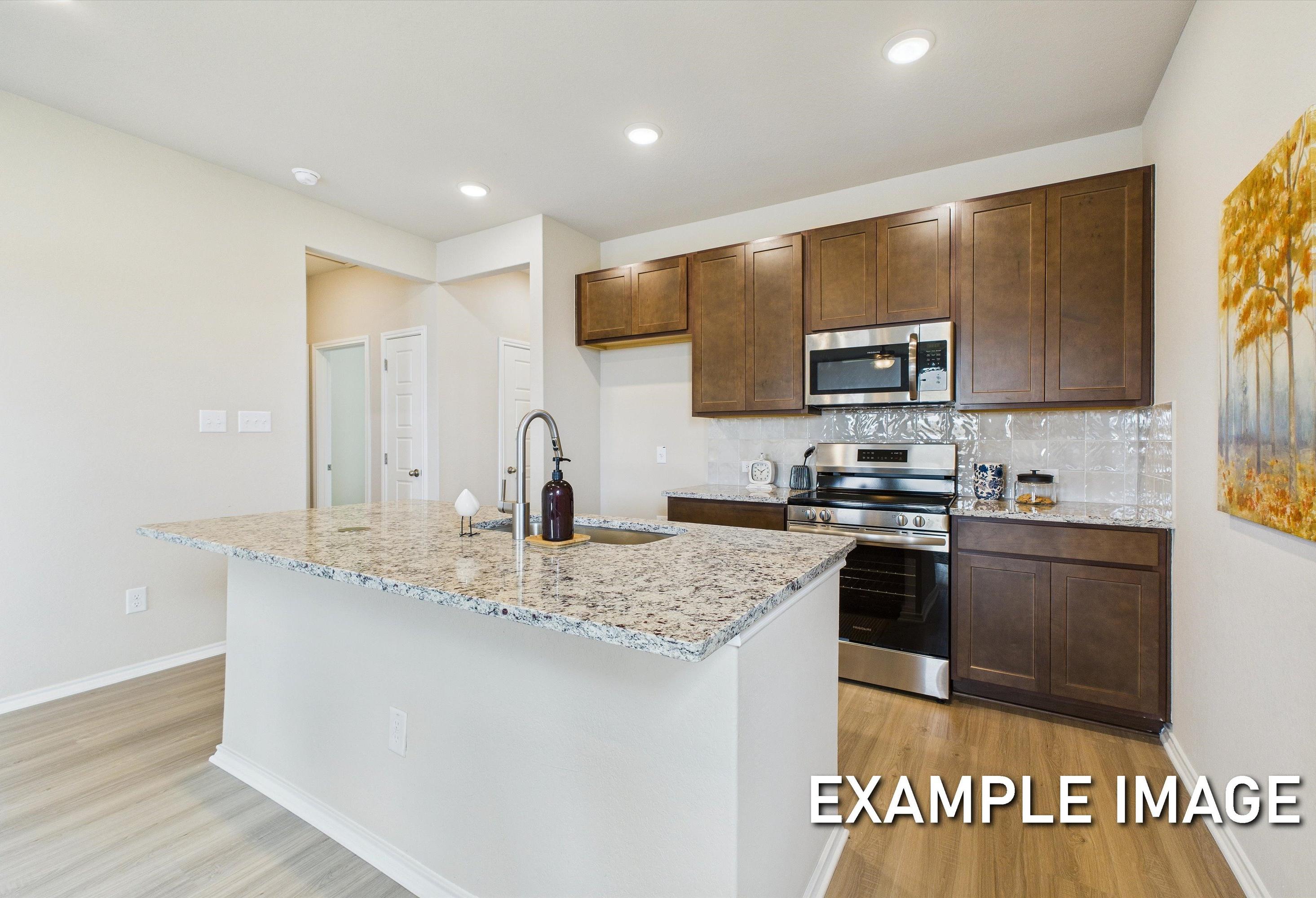 Modern kitchen in The Corral by Davidson Homes featuring granite countertops, dark wood cabinetry, and a spacious island.