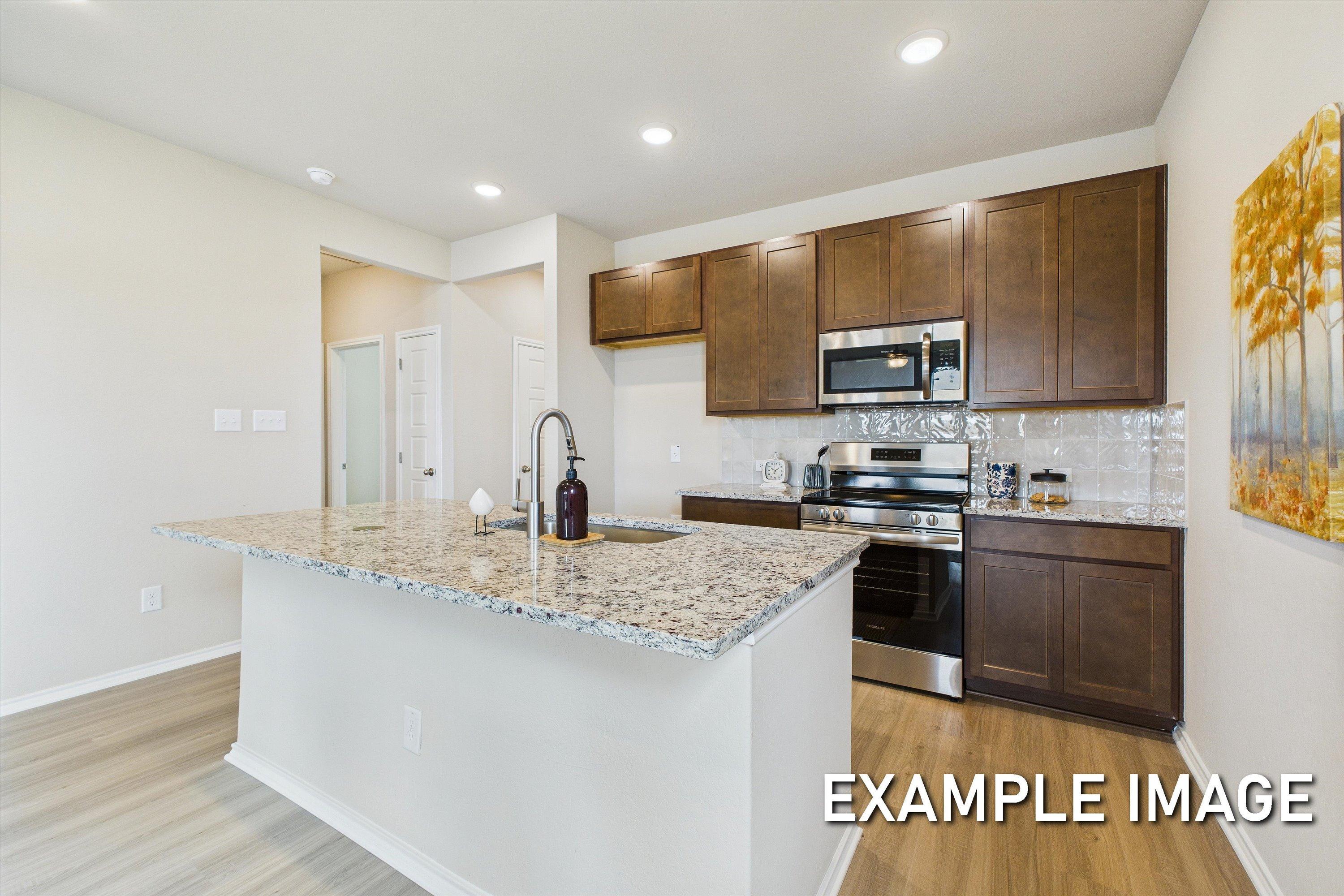 Modern kitchen in The Comal by Davidson Homes featuring granite countertops, dark wood cabinets, and a central island.
