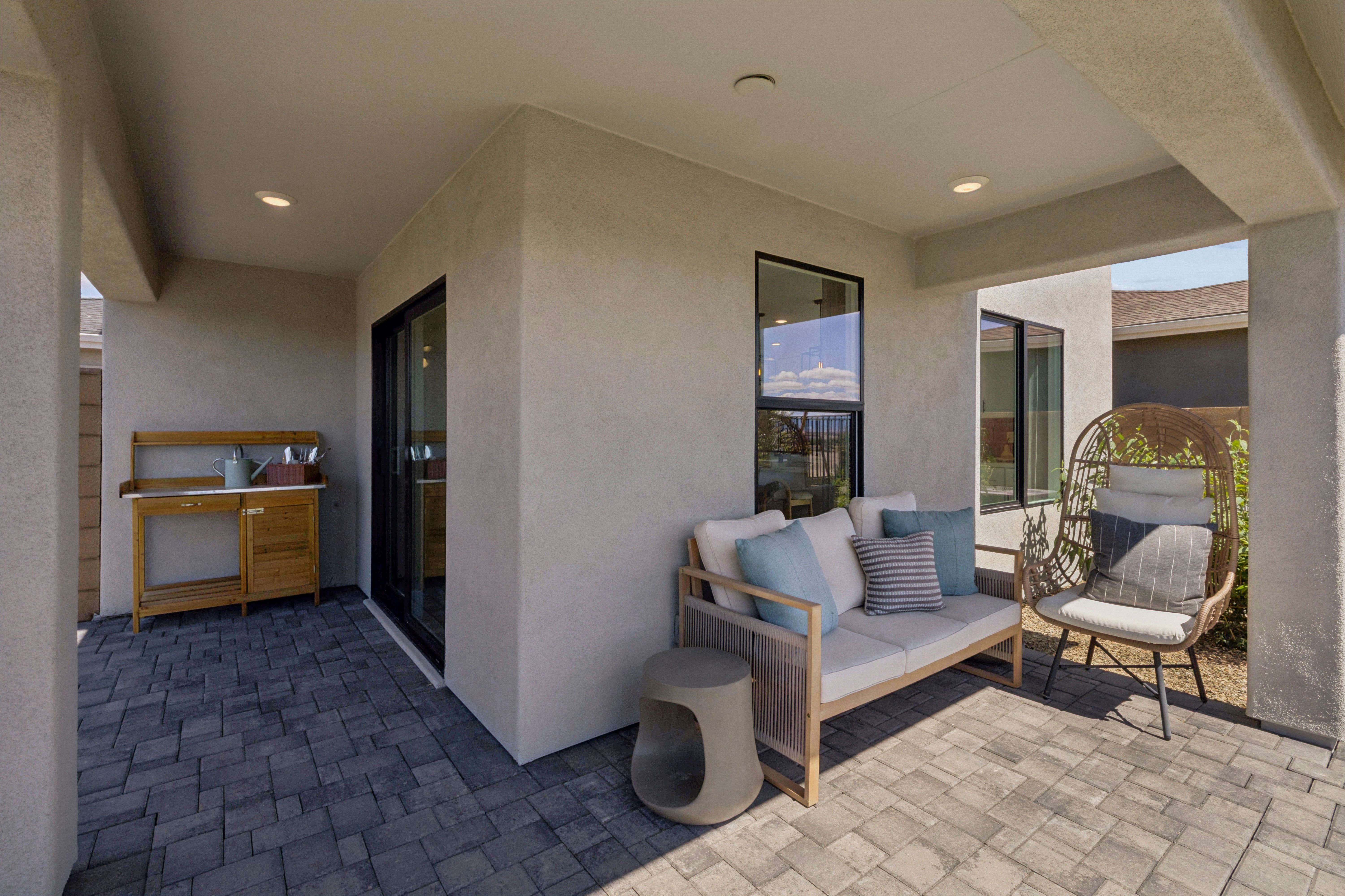 Spacious covered patio at South Ranch Southern Collection in Prescott AZ with beige sofa, rattan hanging chair, and wooden potting bench