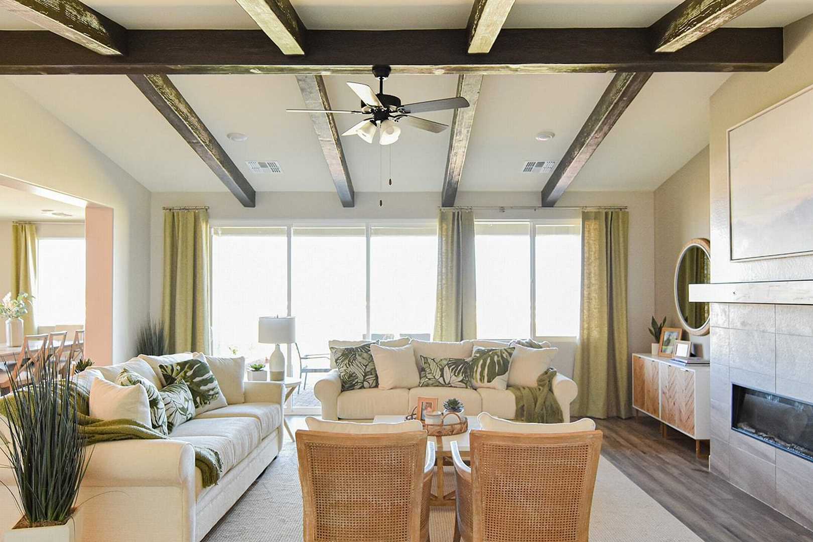 Spacious open-concept living room in The Summit B with exposed beam ceiling, gas fireplace, plush white sofas, and large sunny windows