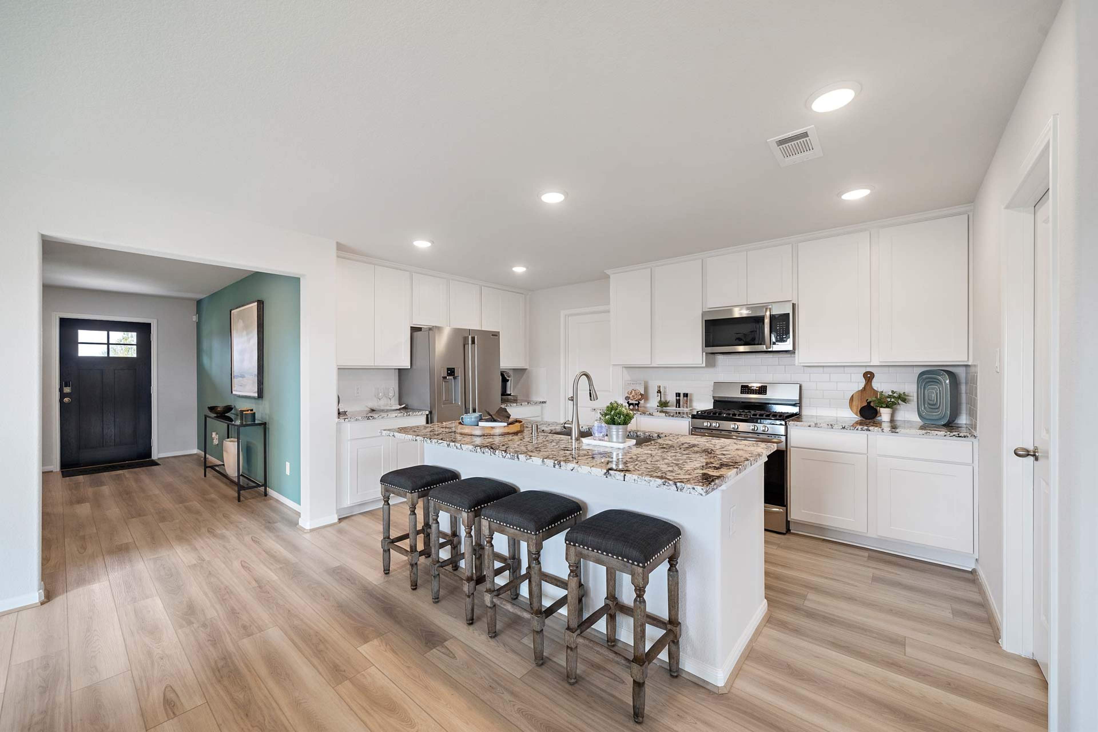Modern open-concept kitchen in Sunterra Katy TX by Davidson Homes featuring white cabinets, granite island with bar seating, stainless appliances, hardwood floors