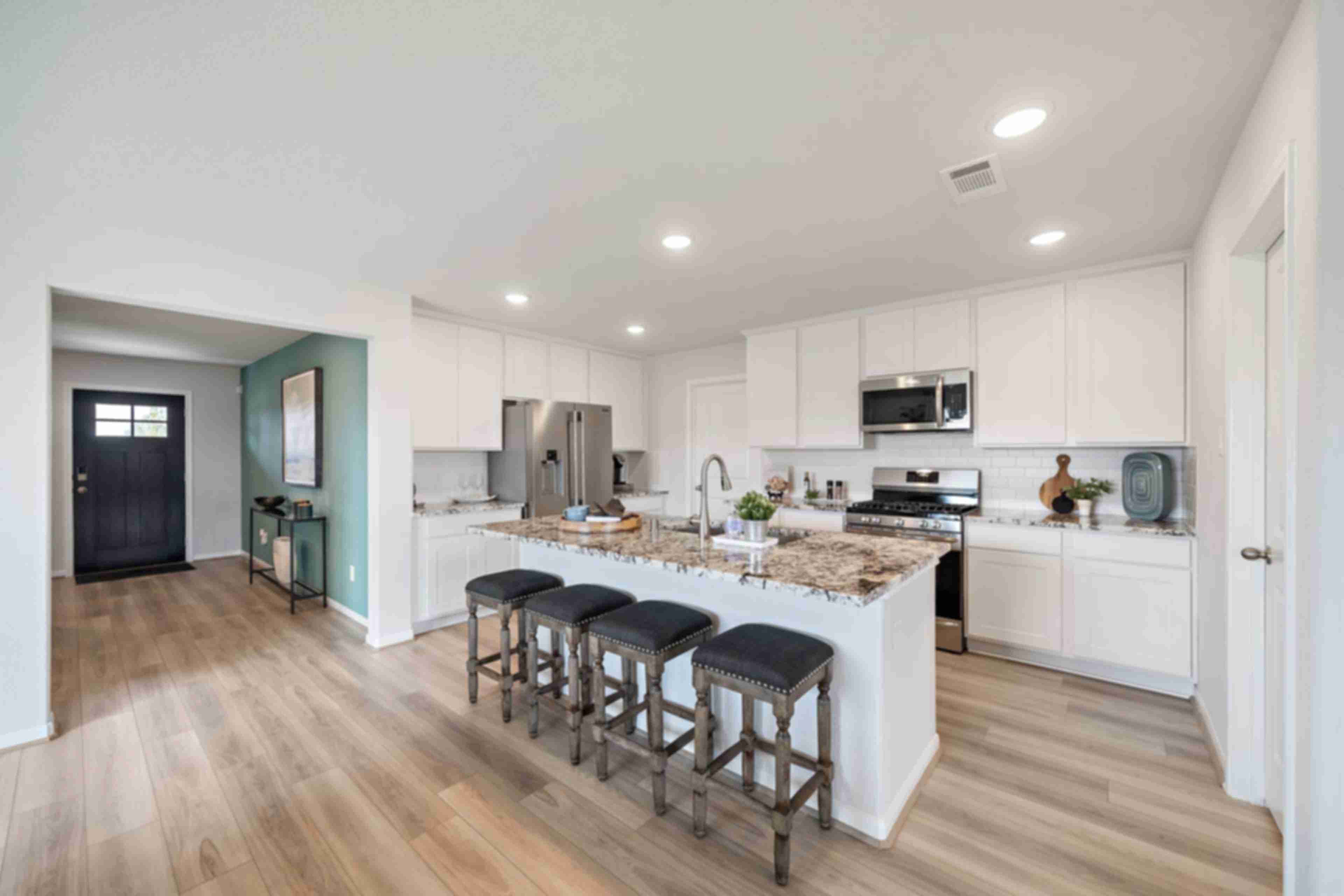 Modern open-concept kitchen in Sunterra Katy TX by Davidson Homes featuring white cabinets, granite island with bar seating, stainless appliances, hardwood floors