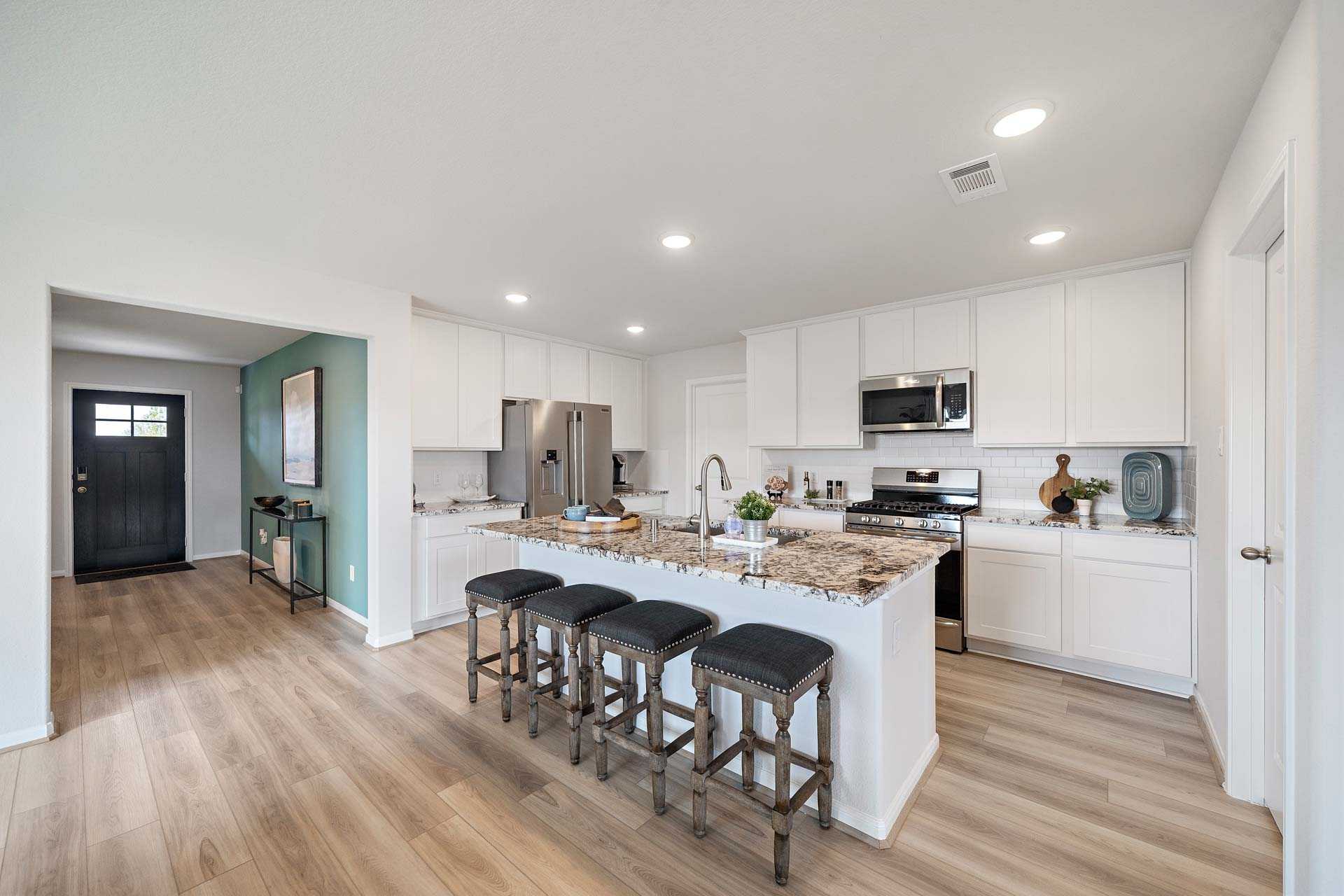 Open-concept kitchen at Sunterra in Katy Texas with white shaker cabinets large granite island bar seating stainless appliances and hardwood floors