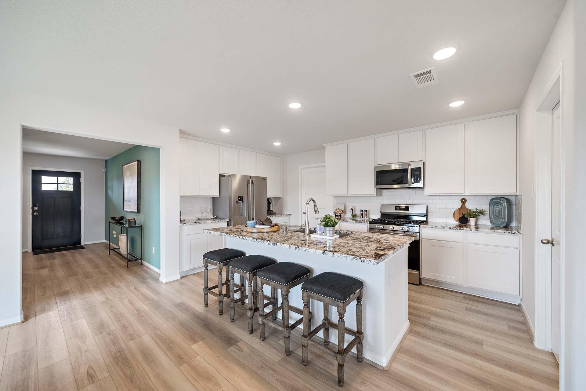 Open-concept kitchen at Sunterra in Katy Texas with white shaker cabinets large granite island bar seating stainless appliances and hardwood floors