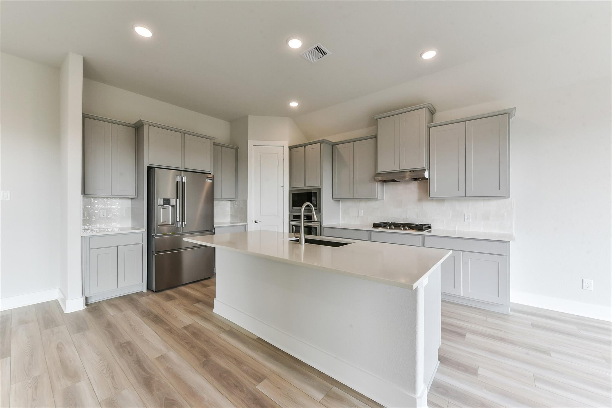 Modern kitchen with gray shaker cabinets, white quartz island, stainless fridge and gas cooktop in Davidson Homes Edward A, Texas City