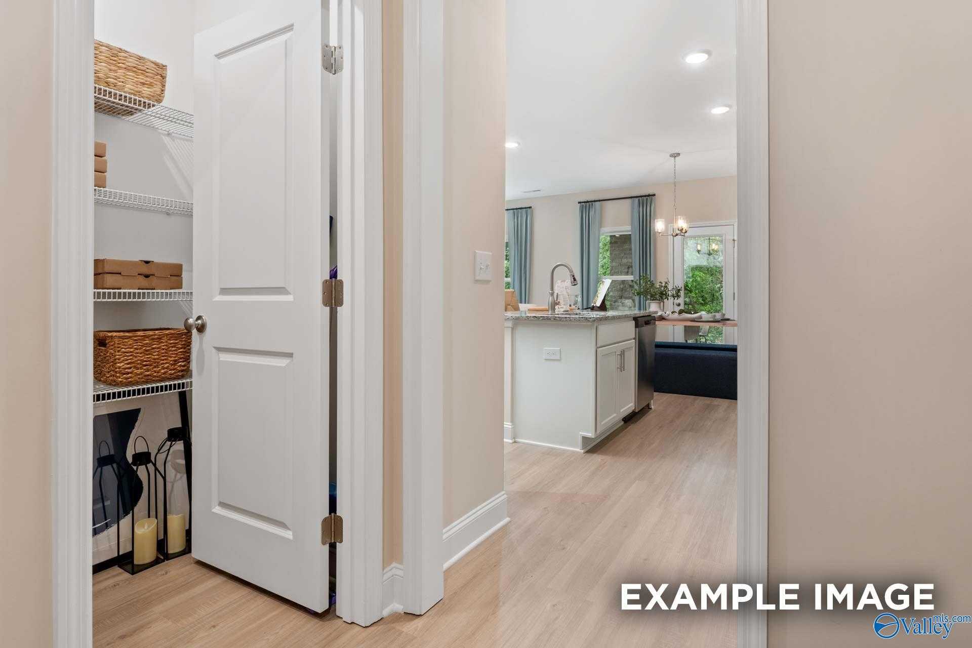 Well-organized pantry with shelves, baskets and storage bottles next to modern kitchen island in The Camden B, Huntsville, Alabama