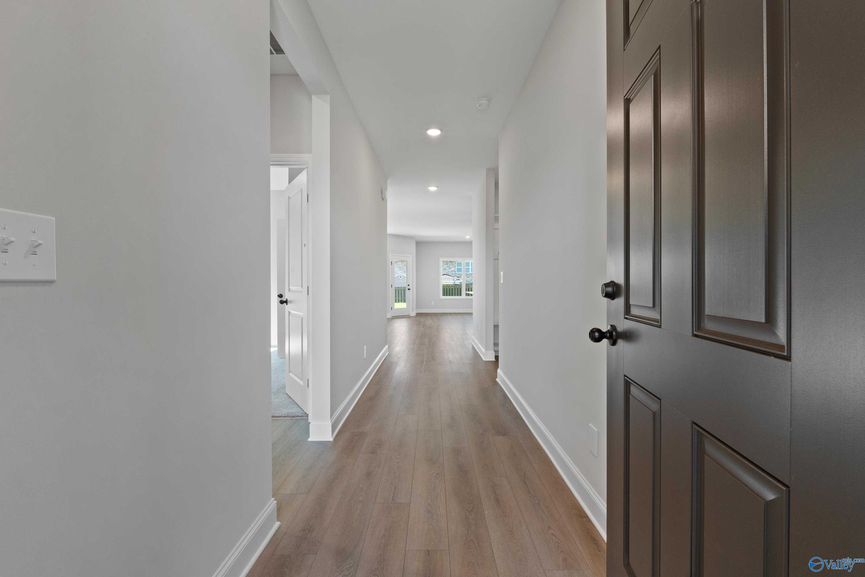 Bright hallway with light hardwood floors, white walls, and interior doors in Davidson Homes The Franklin C, Hazel Green, Alabama