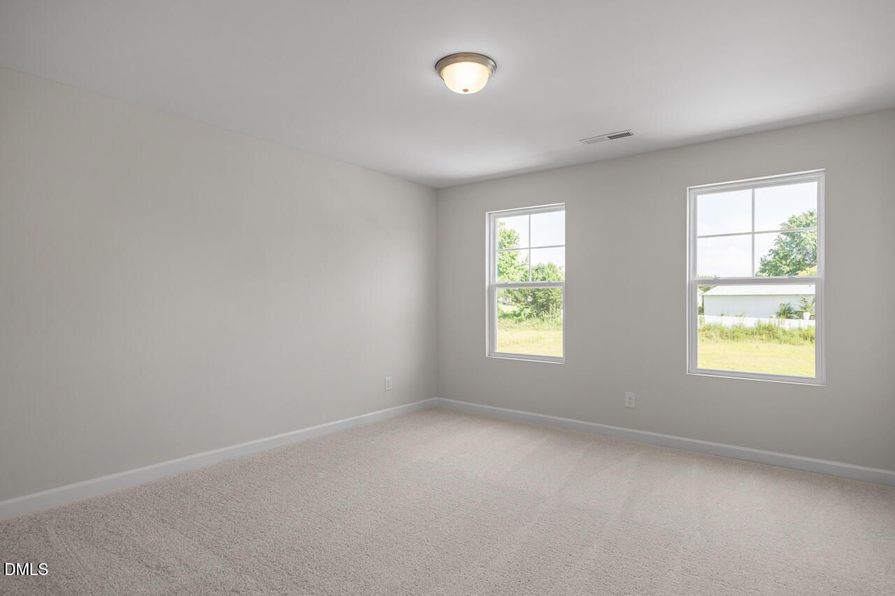 Bright secondary bedroom with gray walls, carpet floor, and large windows overlooking lawn in The Preston A, Lillington, NC
