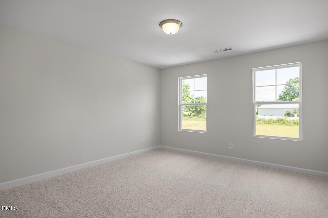 Bright secondary bedroom with gray walls, carpet floor, and large windows overlooking lawn in The Preston A, Lillington, NC