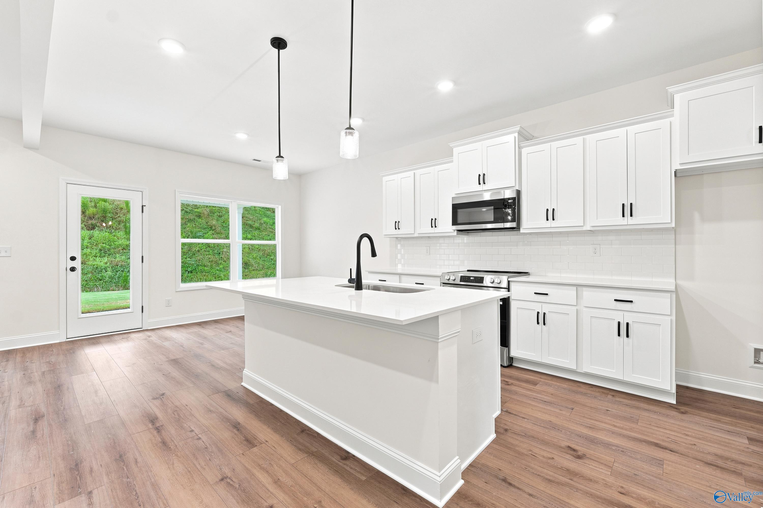 Modern white kitchen with island, pendant lighting, and stainless steel appliances in The Shelby D home in Cullman, Alabama.