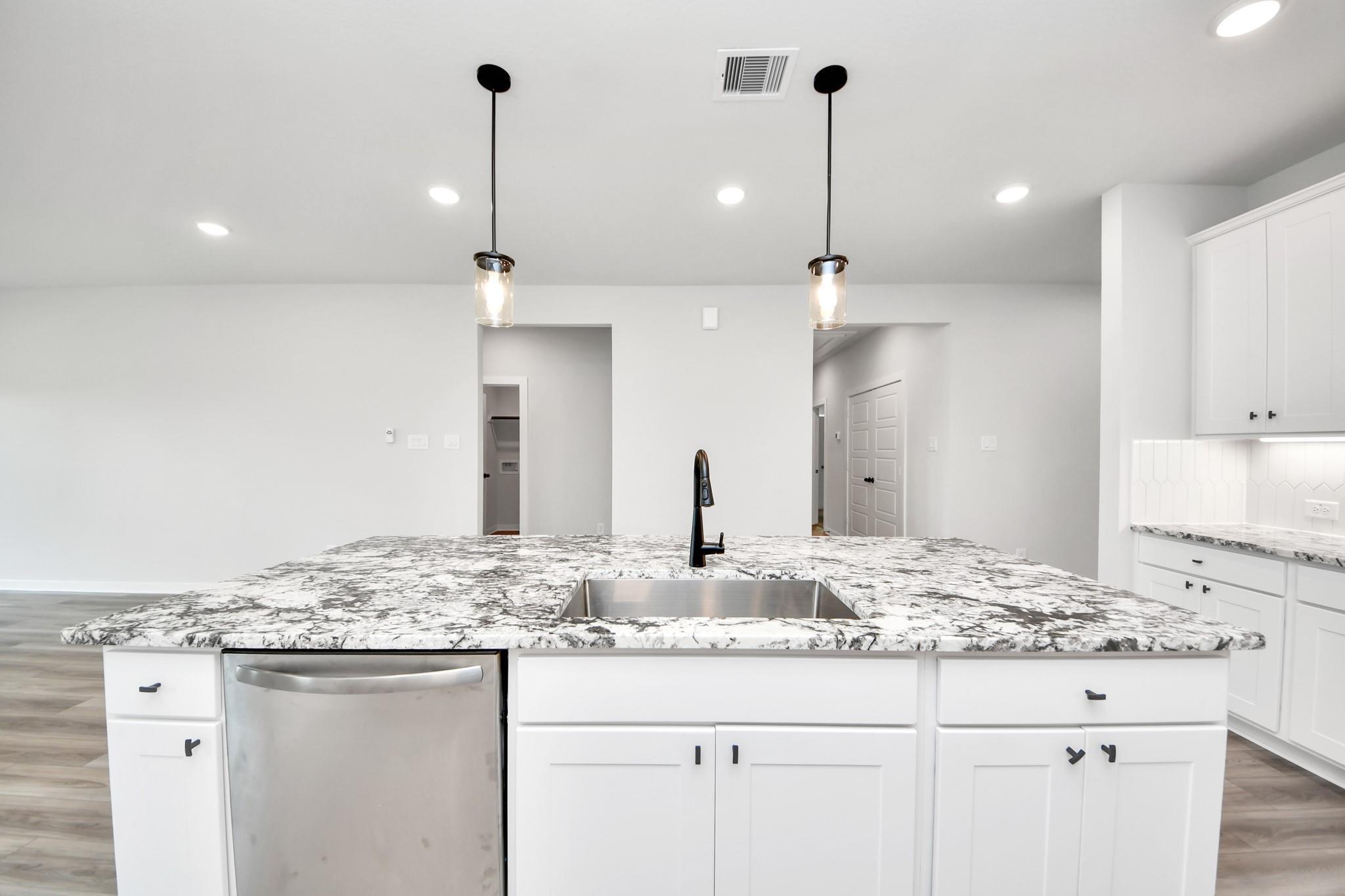 Modern kitchen island with granite countertops and pendant lighting in The Sorrento E floor plan at Sundance Cove, Crosby.
