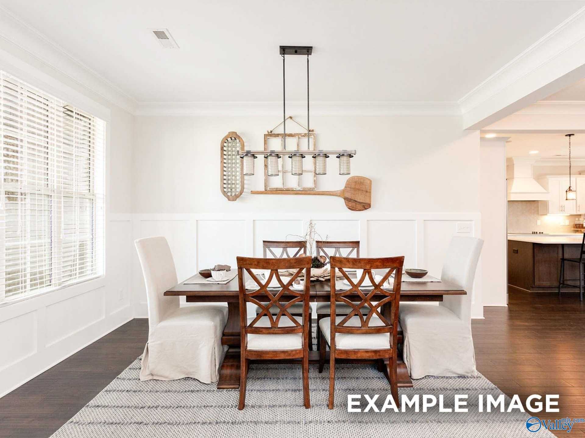 Elegant dining room with wood table, chandelier, wainscoting walls, and open kitchen view in Davidson Homes The Finleigh, Meridianville, Alabama