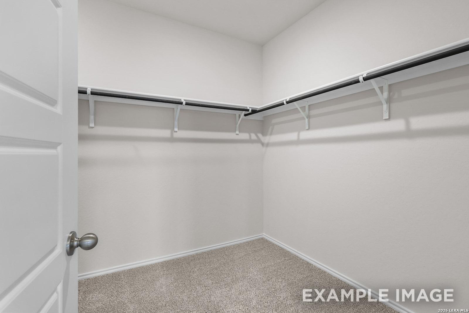Walk-in closet with neutral carpeting and built-in shelving in The Sequoia C floor plan by Davidson Homes in San Antonio.