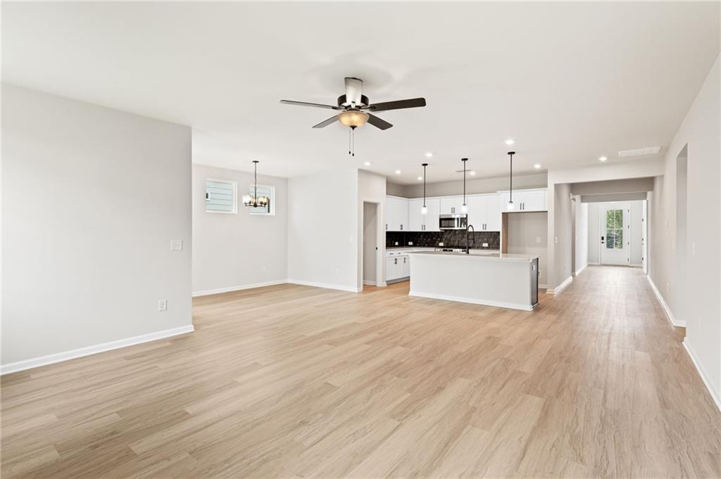 Open-concept kitchen and living area with white cabinets, large island, ceiling fan, hardwood floors in The Daphne C, Loganville, GA