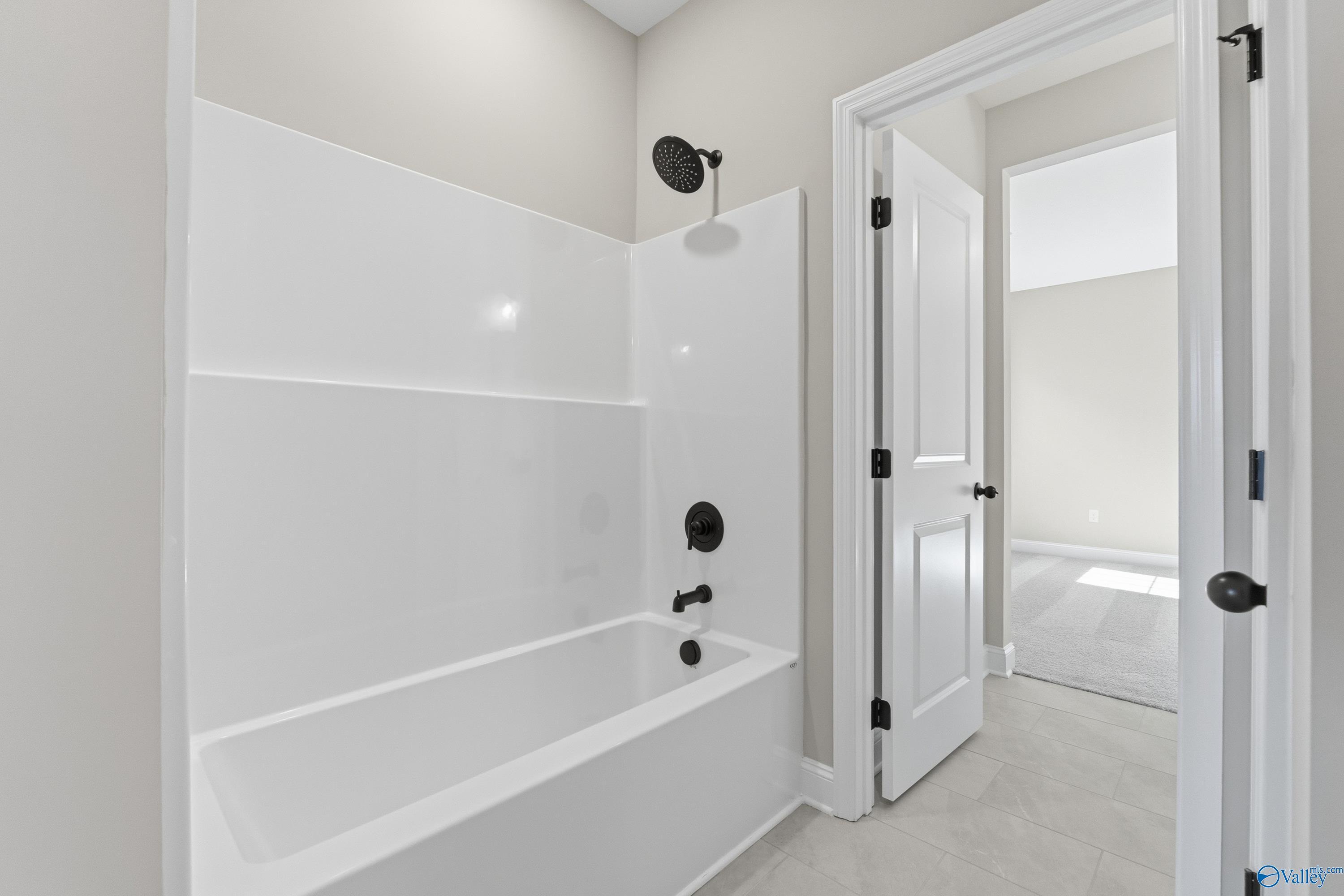 Modern bathroom featuring white tub, glass shower enclosure, and rainfall showerhead in Davidson Homes The Finleigh, Meridianville, Alabama