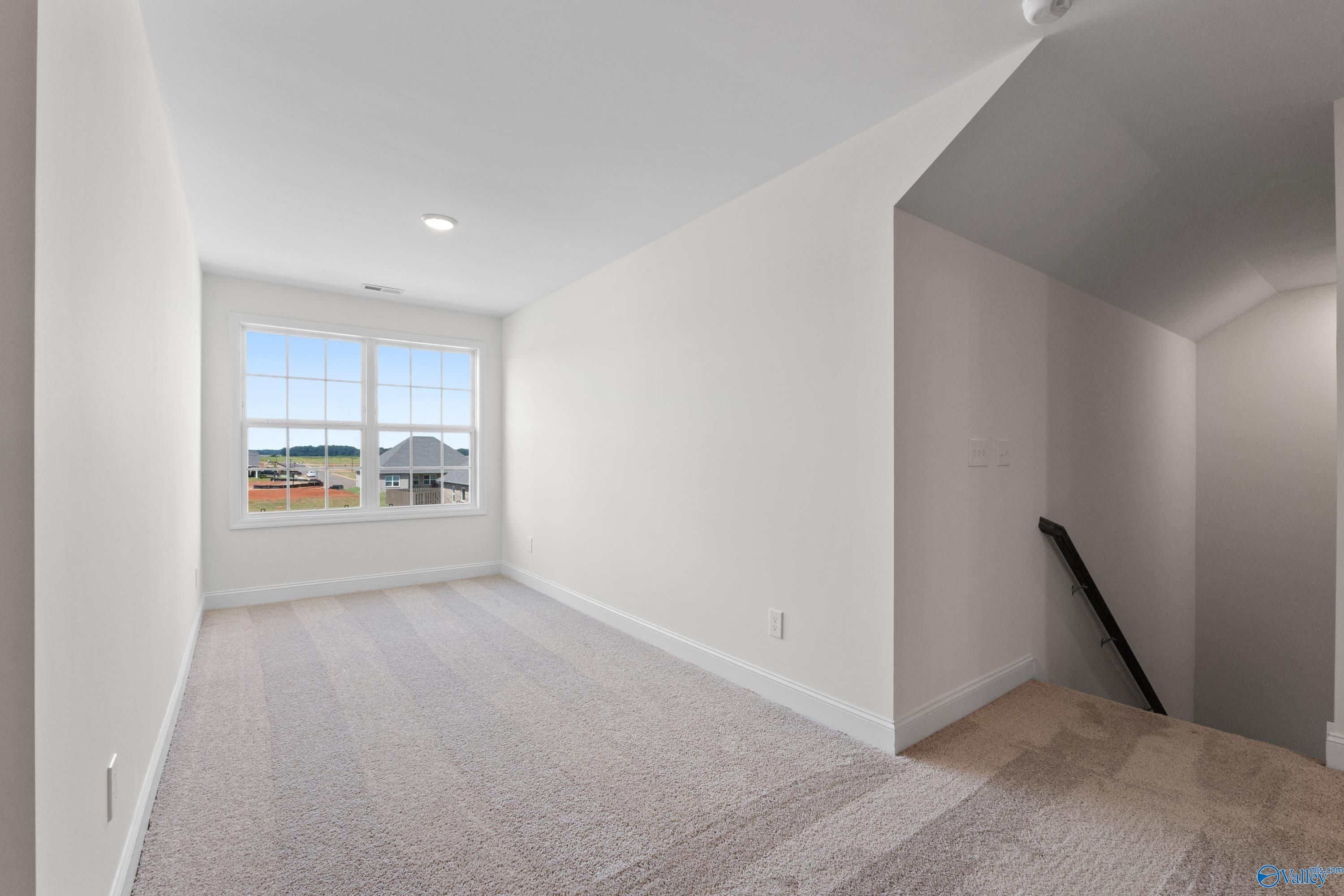 Spacious bonus room with large window, beige carpet, and staircase in Davidson Homes The Rockford B, Toney, Alabama