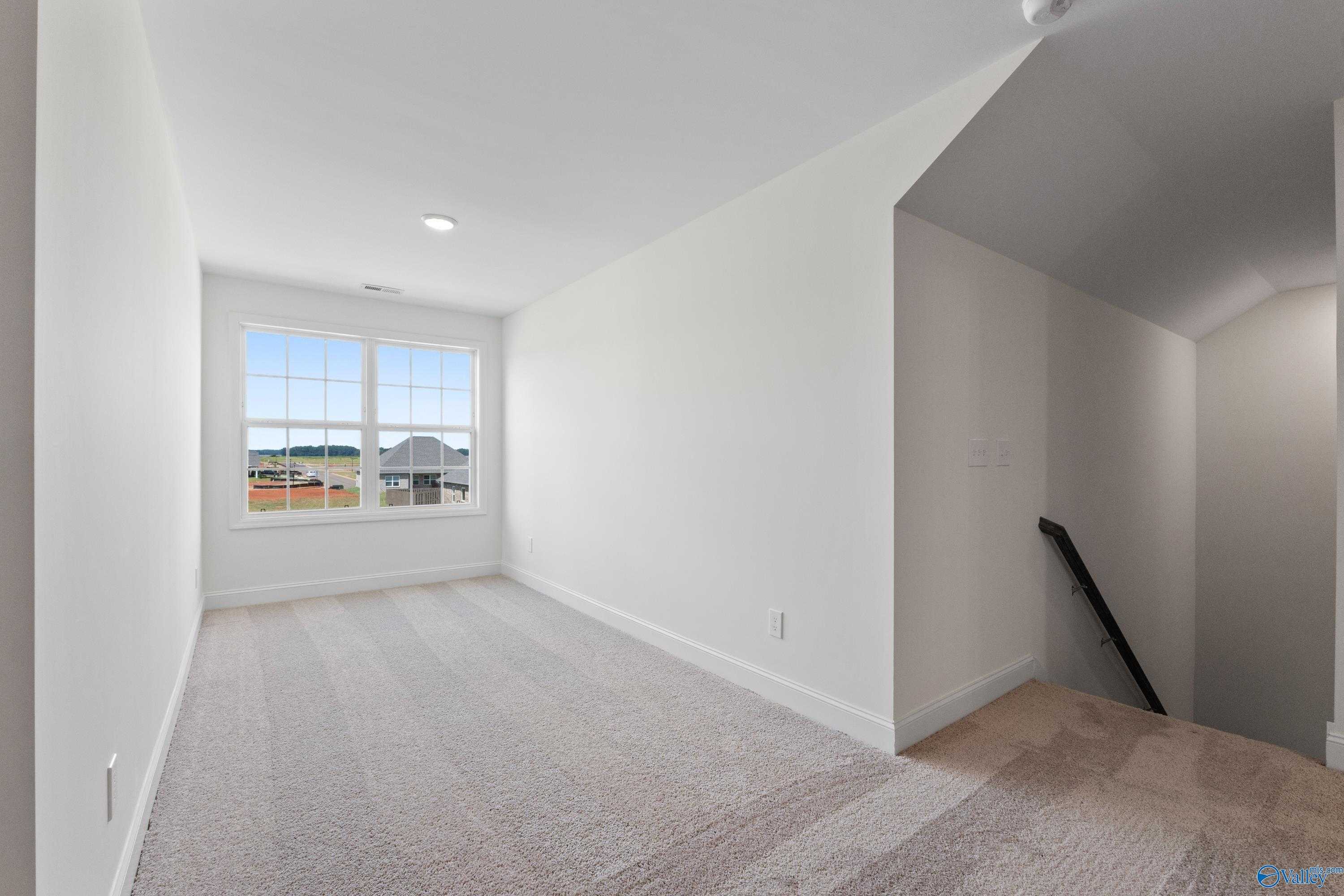 Spacious bonus room with large window, beige carpet, and staircase in Davidson Homes The Rockford B, Toney, Alabama