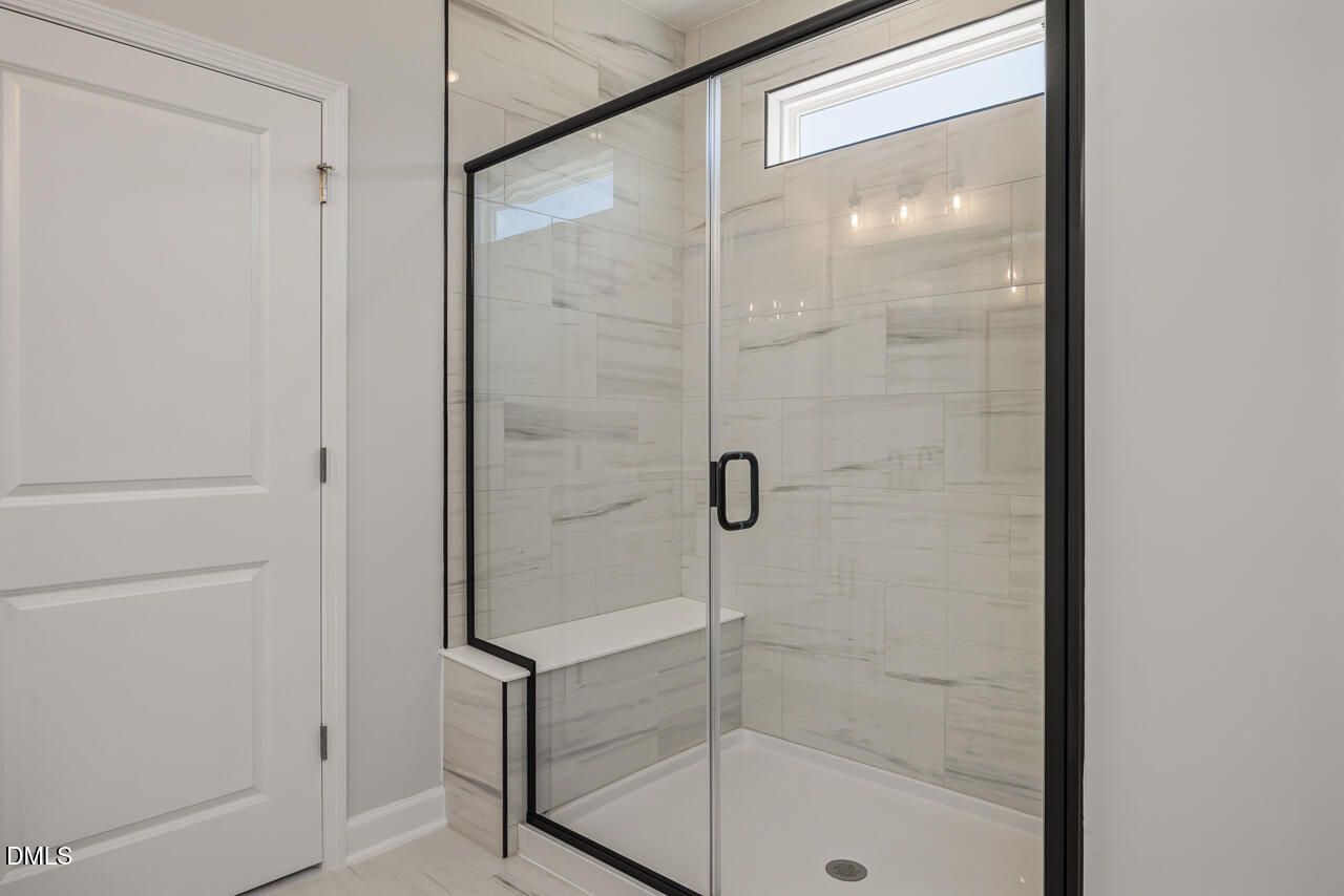 Modern walk-in shower with marble-look tile and black frame in The Birch II E home at Sage on North Main, Wake Forest.