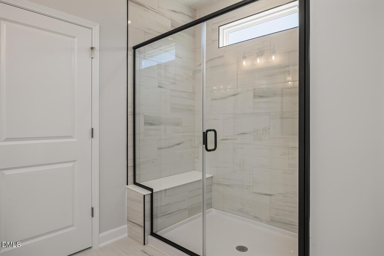 Modern walk-in shower with marble-look tile and black frame in The Birch II E home at Sage on North Main, Wake Forest.