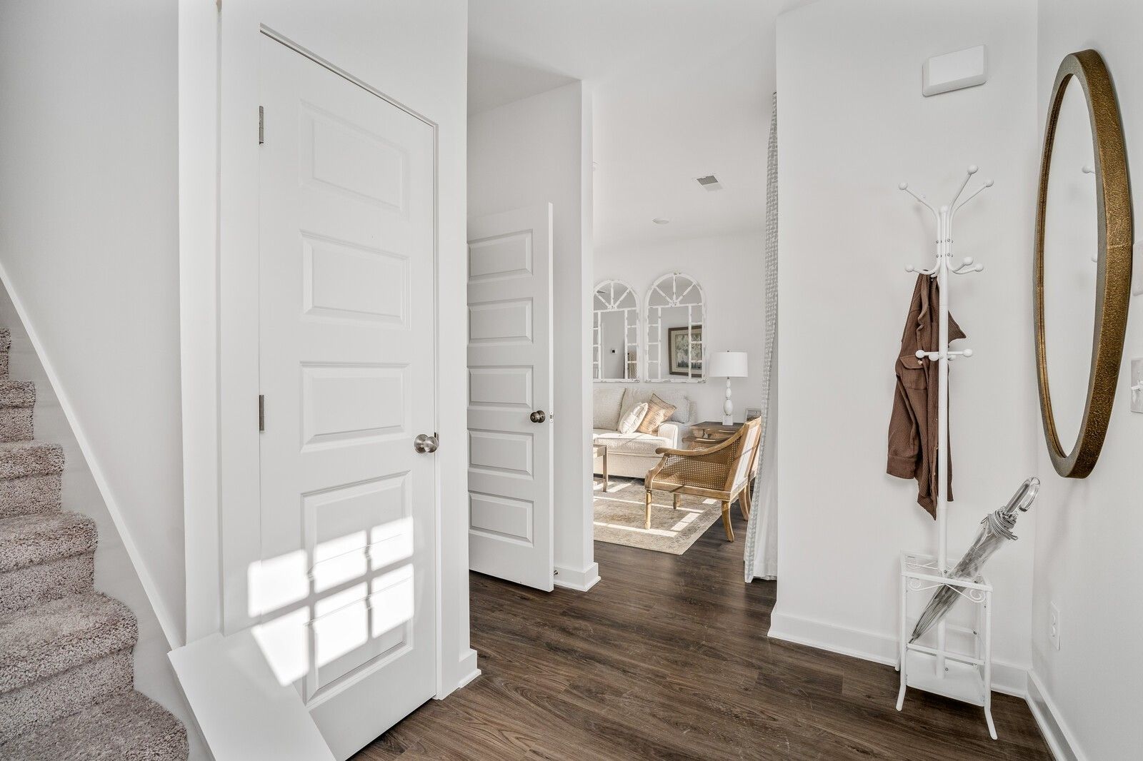 Bright foyer with white doors, wood floors, coat rack, gold mirror, carpeted stairs, and cozy living room in Davidson Homes Cumberland A, Gallatin TN