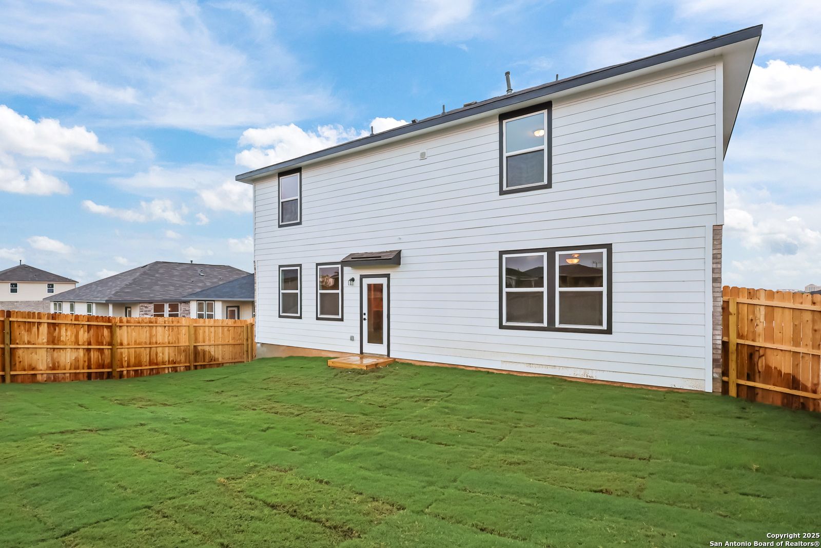 Rear view of two-story Davidson Homes Douglas F with covered patio, green lawn, and wooden fence in Comanche Ridge, San Antonio