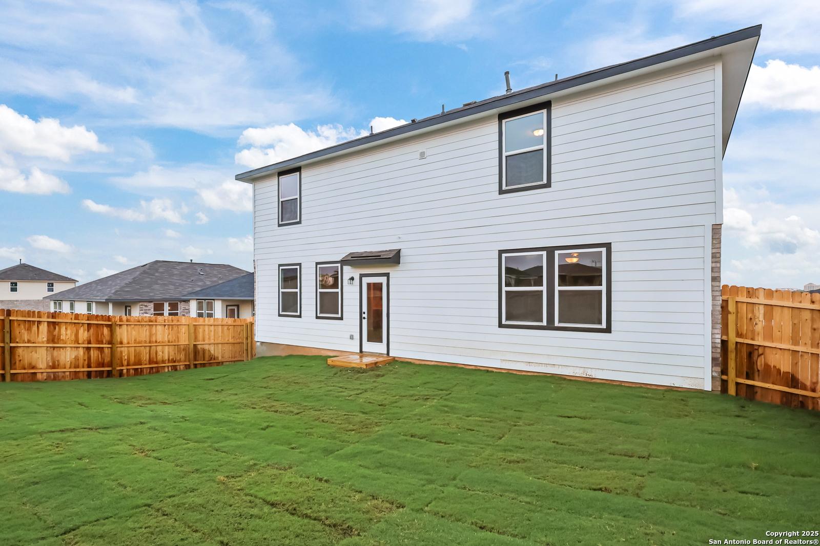 Rear view of two-story Davidson Homes Douglas F with covered patio, green lawn, and wooden fence in Comanche Ridge, San Antonio