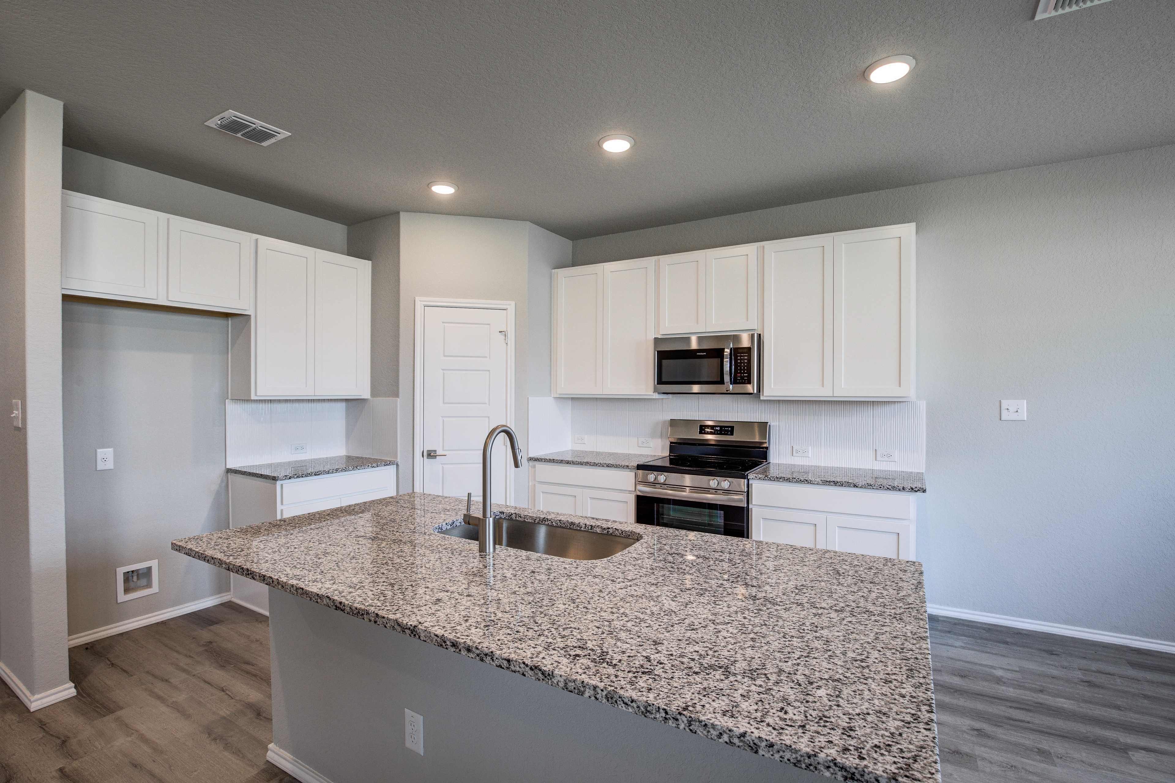 Spacious kitchen in The Asheville home design with white shaker cabinets, granite island sink, stainless steel appliances