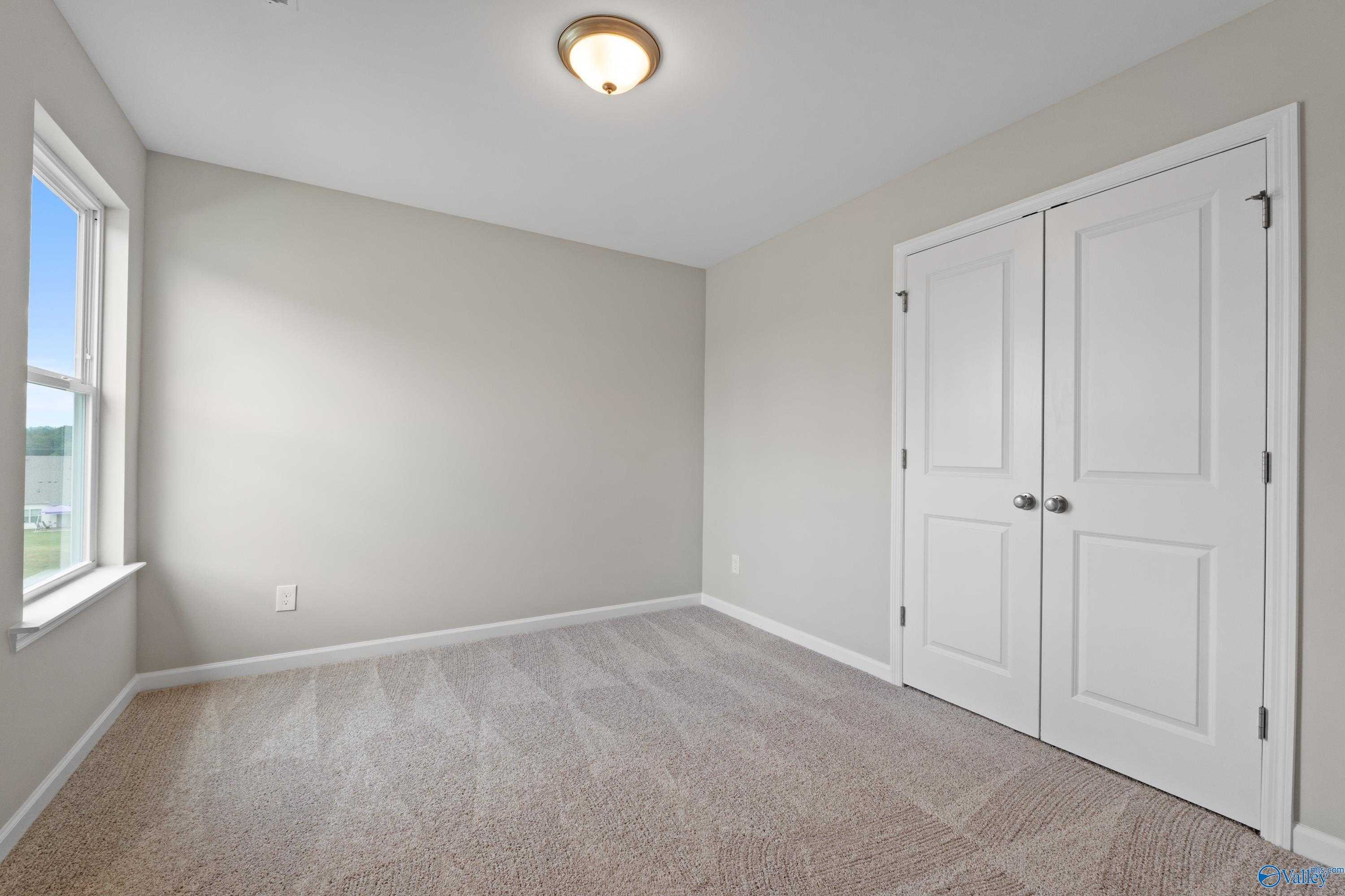 Bright secondary bedroom with neutral walls, carpet floor, double closet doors, and sunny window in Evermore Homes The Augusta, Madison AL