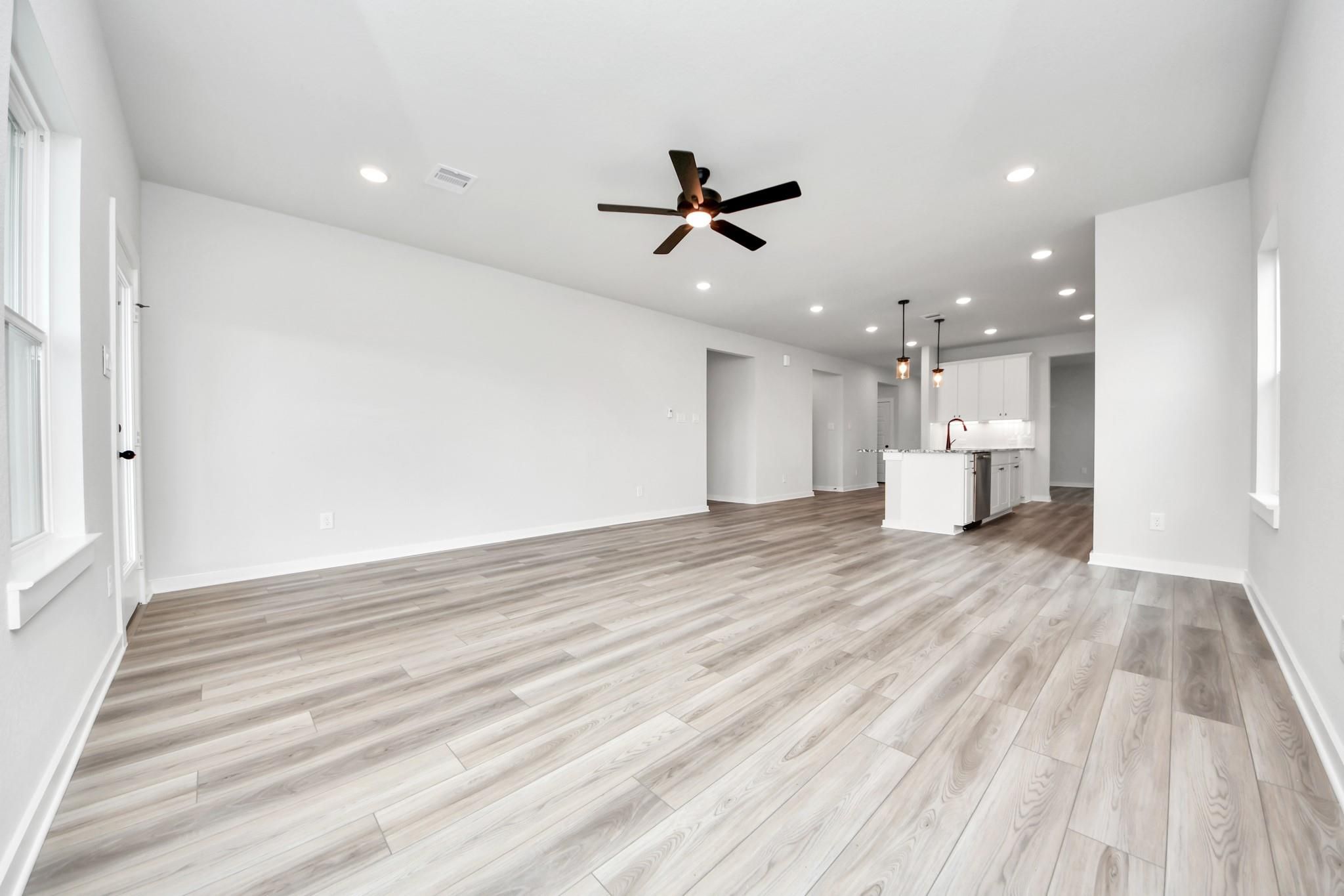 Open-concept living room with wood-look flooring and kitchen view in The Sorrento E floor plan at Sundance Cove, Crosby.