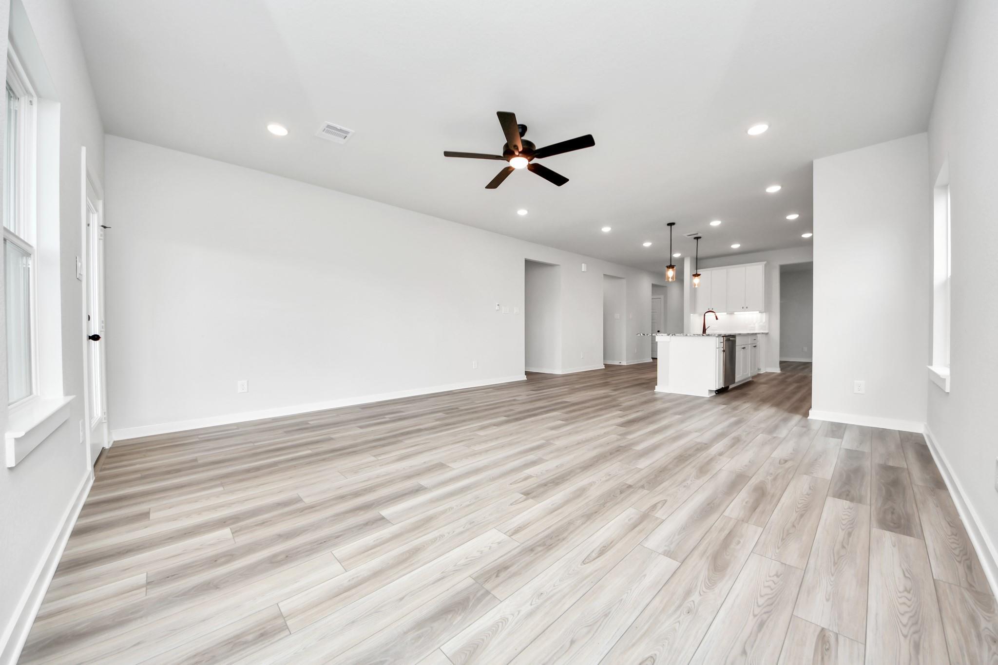 Open-concept living room with wood-look flooring and kitchen view in The Sorrento E floor plan at Sundance Cove, Crosby.