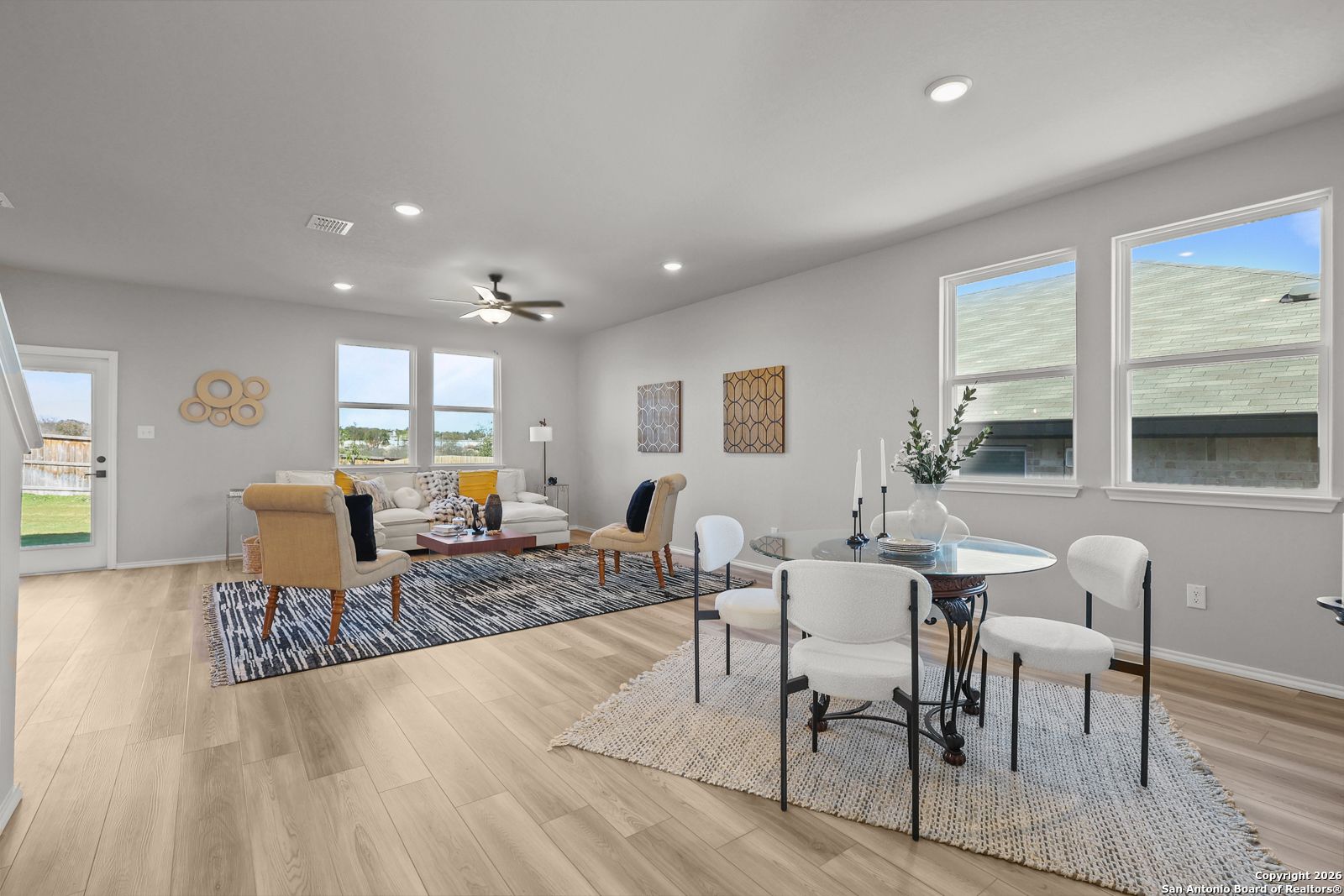 Bright living room with beige sectional sofa, round dining table, ceiling fan, and large windows in Davidson Homes The Murray K, San Antonio