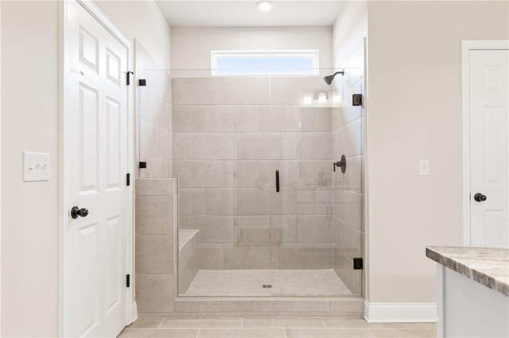 Frameless glass shower with beige tile walls, built-in bench, and modern fixtures in master bath of The Harrison H by Davidson Homes in Winder, Georgia