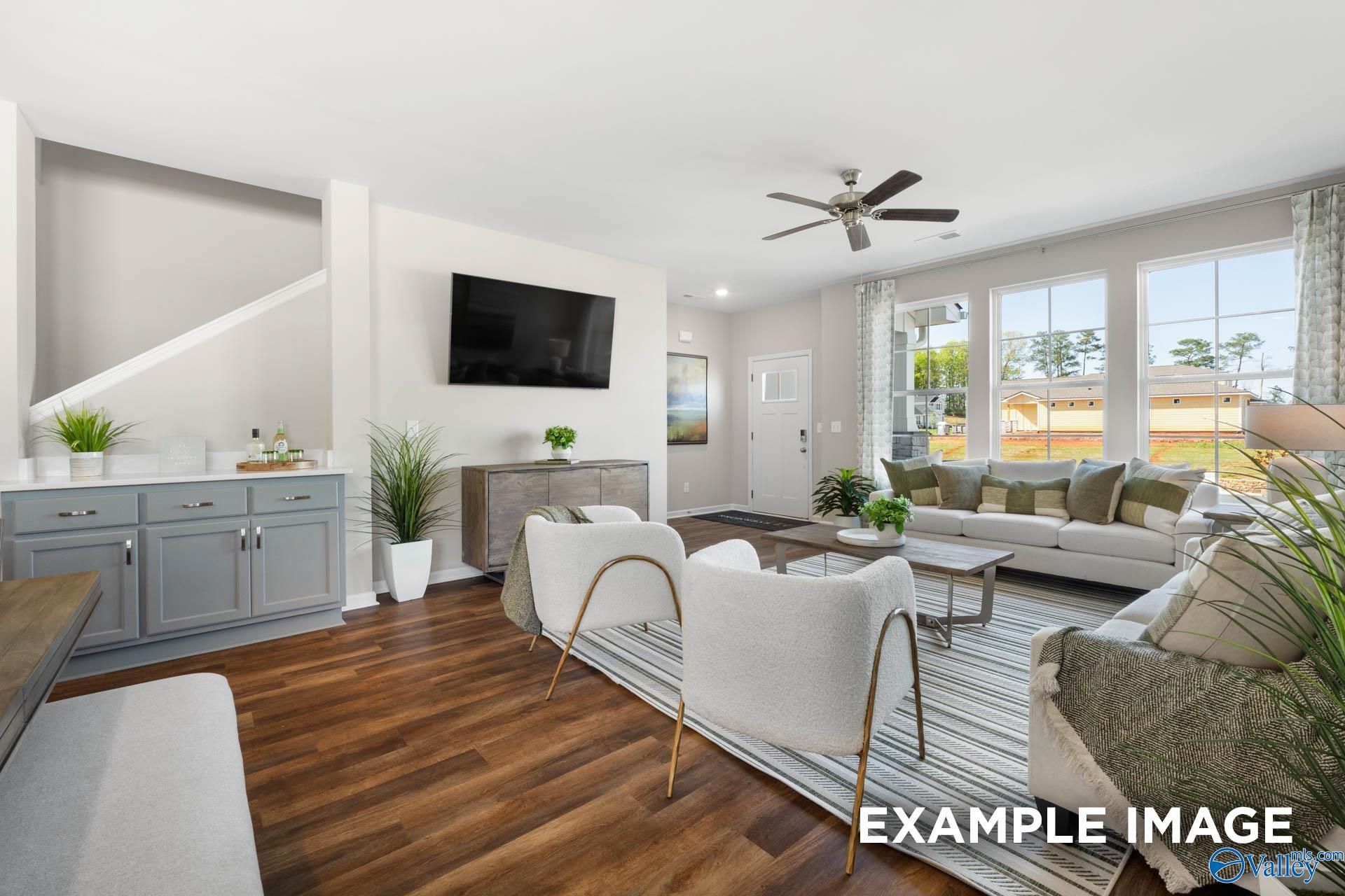 Bright living room with hardwood floors, mounted TV, ceiling fan, plants, and large windows in Davidson Homes The Stella, Madison AL