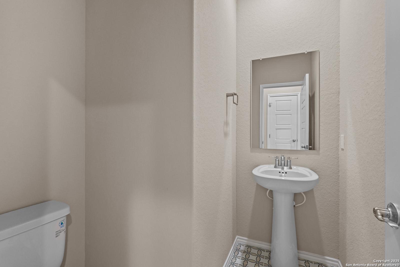 Elegant powder room featuring pedestal sink, toilet, and mirrored vanity in Davidson Homes The Douglas G, San Antonio, Texas
