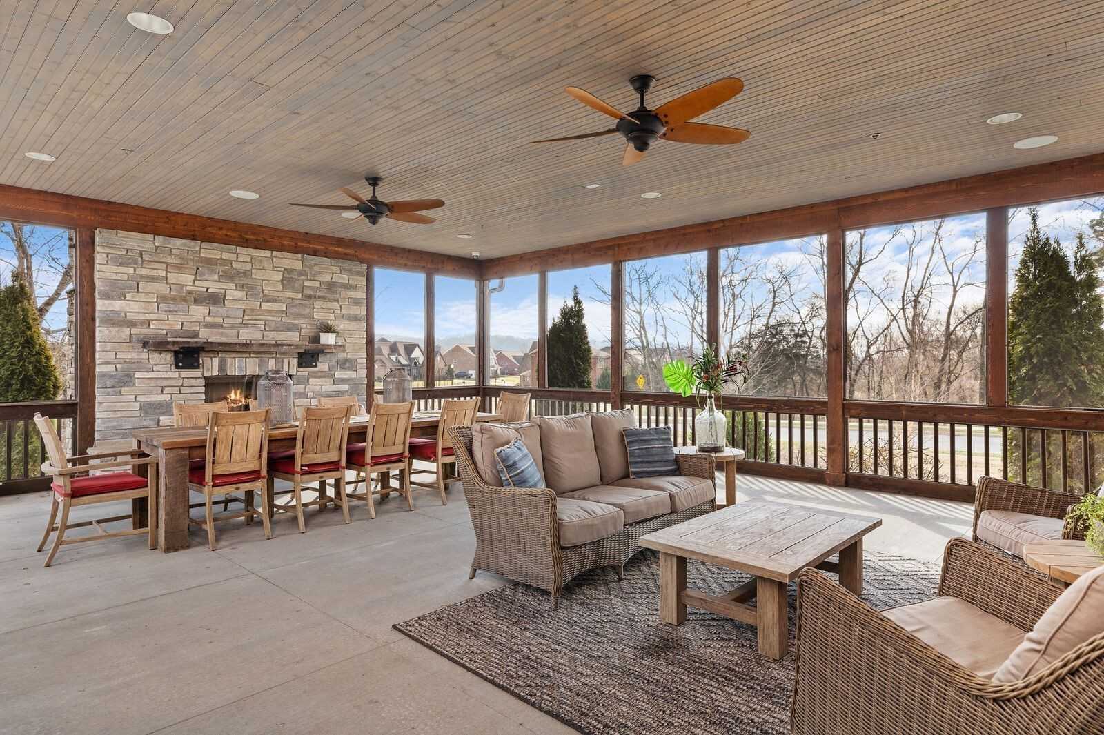 Screened porch with stone fireplace, wooden dining table, cozy sofa seating, and wooded views in Davidson Homes The Ridgeport, Gallatin, TN