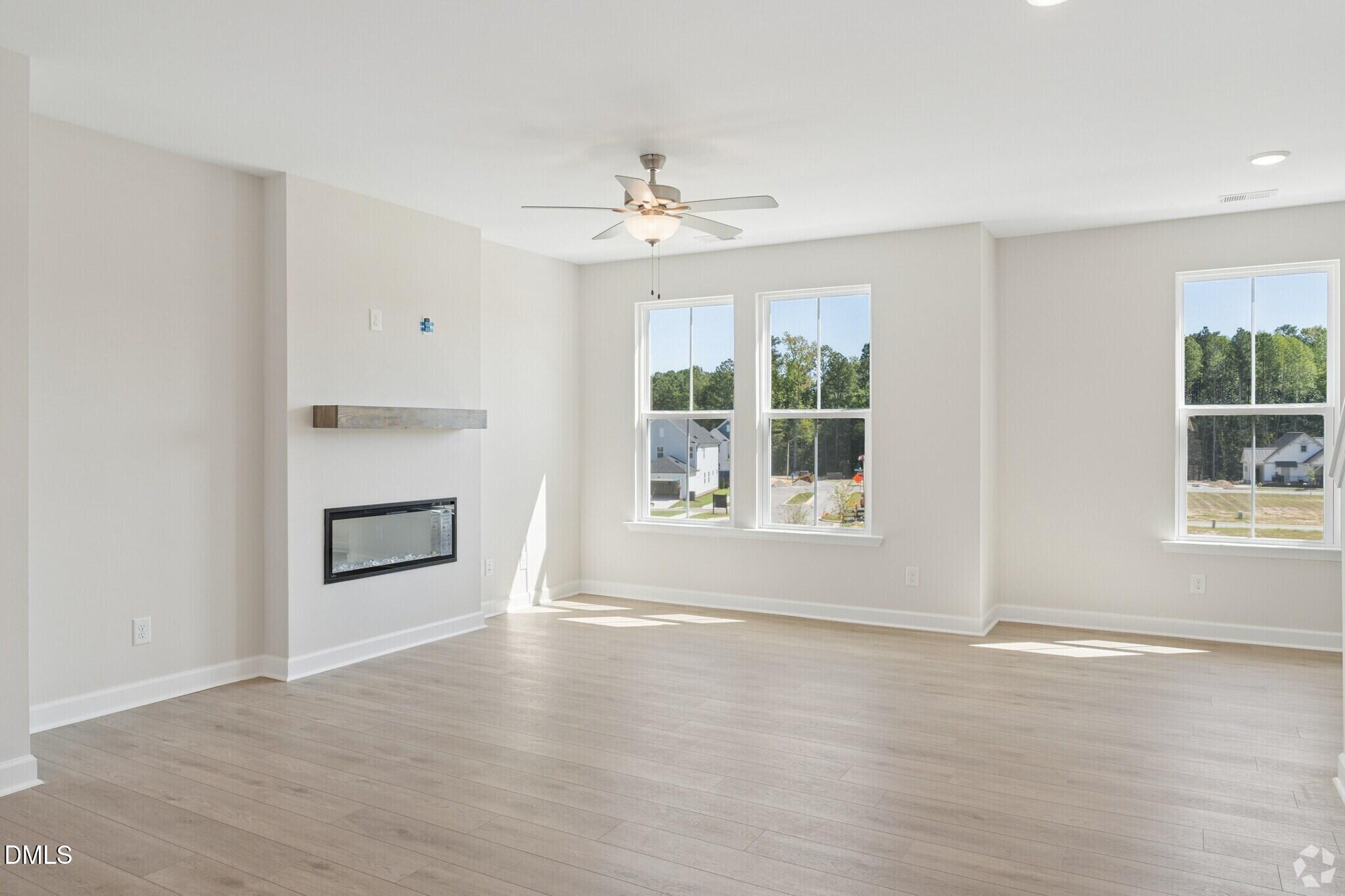 Bright living room with electric fireplace, ceiling fan, and large windows in Davidson Homes The Avery townhome, Knightdale, NC