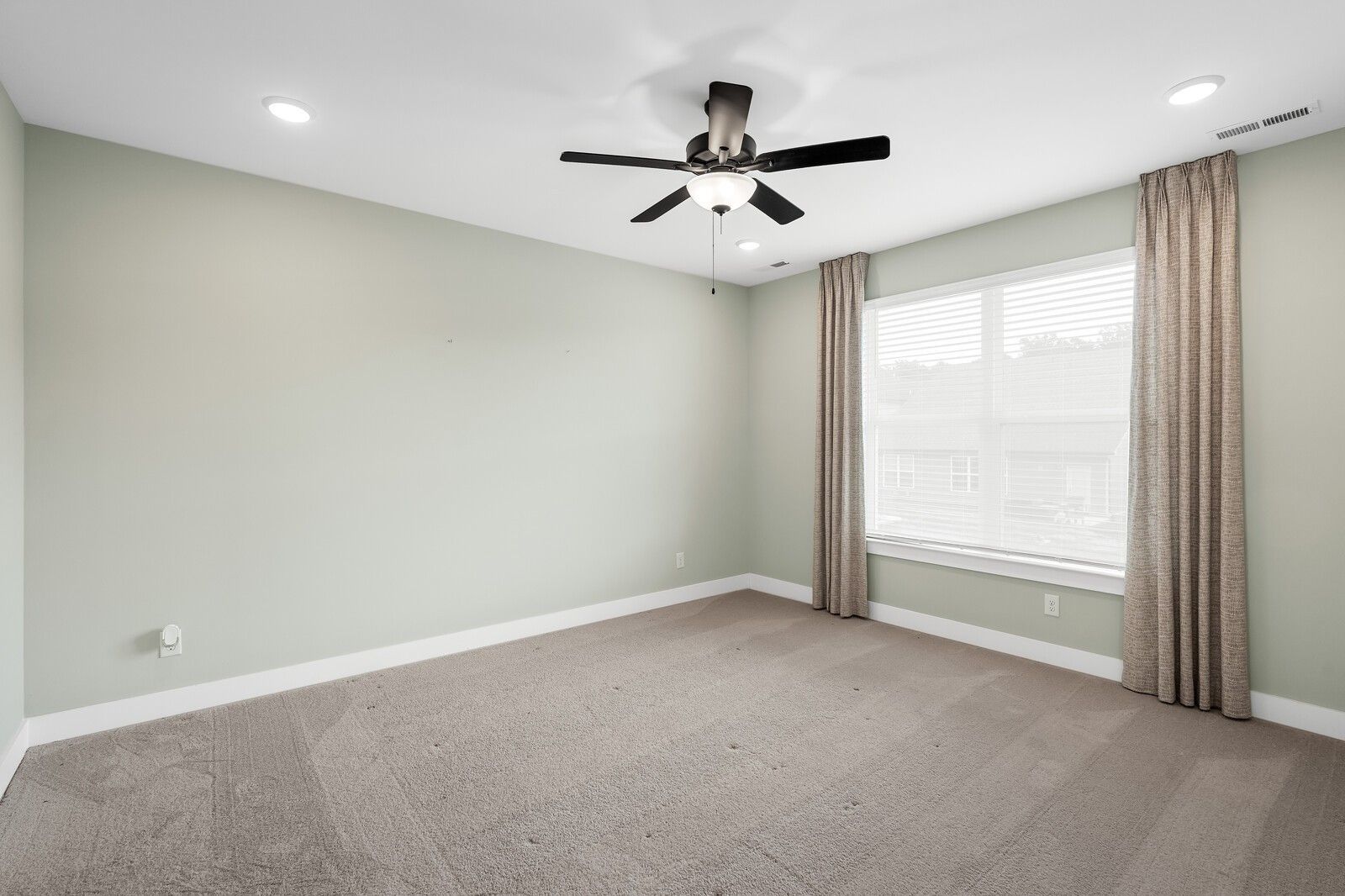 Bright secondary bedroom with ceiling fan, large curtained window, and pale green walls in Davidson Homes The Ridgeport, Gallatin, TN